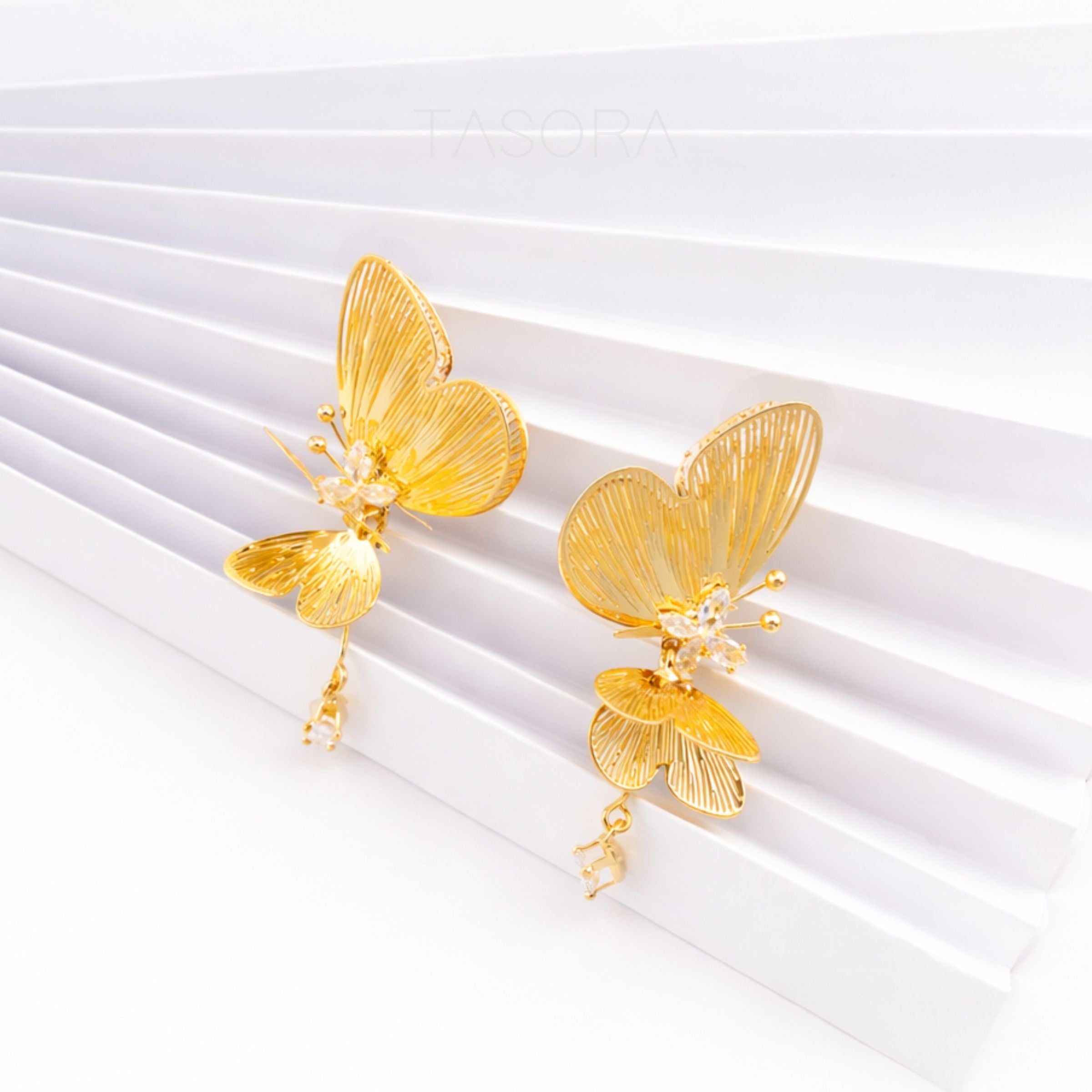 Gold butterfly earrings on a white background with Tasora Branding