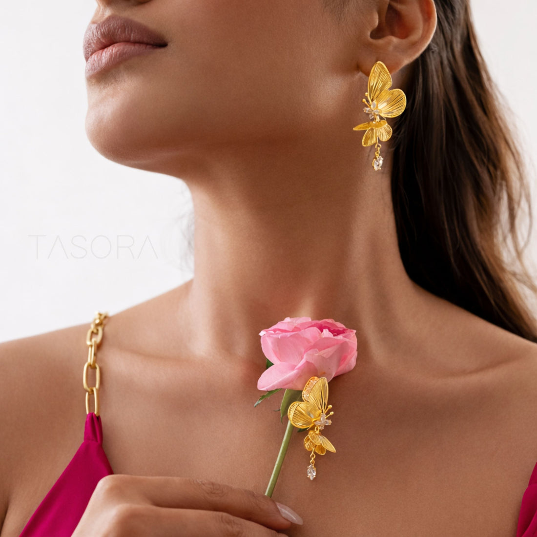 Gold butterfly earrings with a clear gemstone on a white background, branded 'TASORA'.