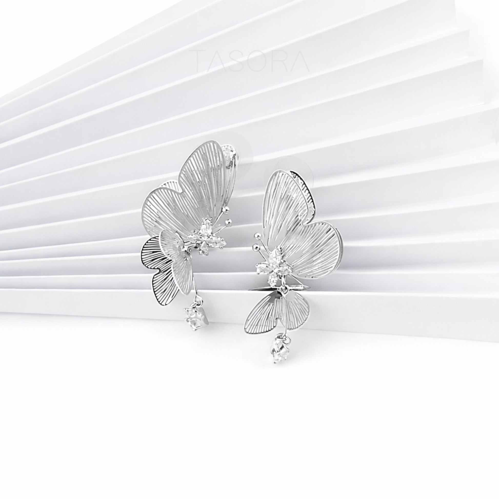 Silver butterfly earrings on a white paper background with TASORA branding