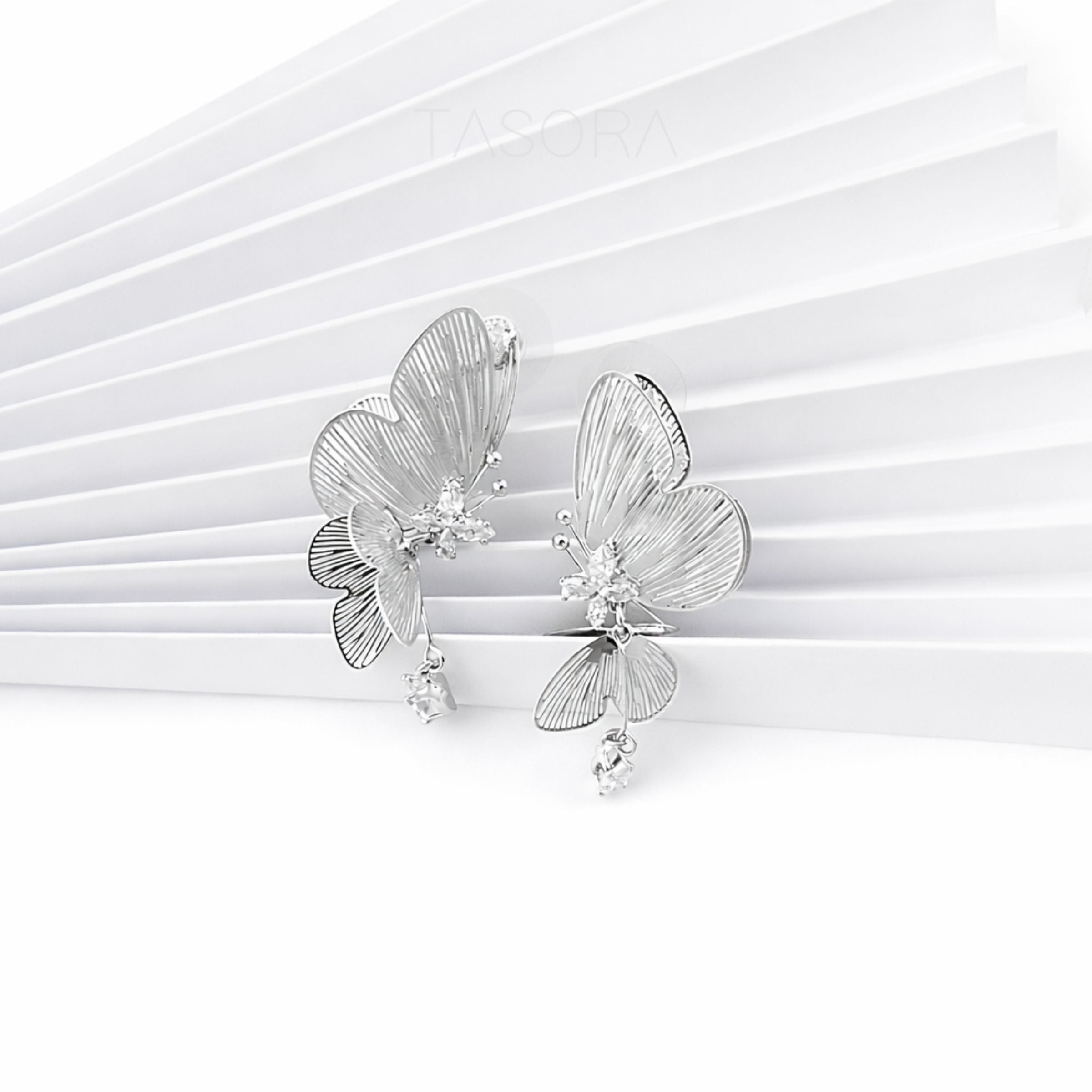 Silver butterfly earrings on a white paper background with TASORA branding