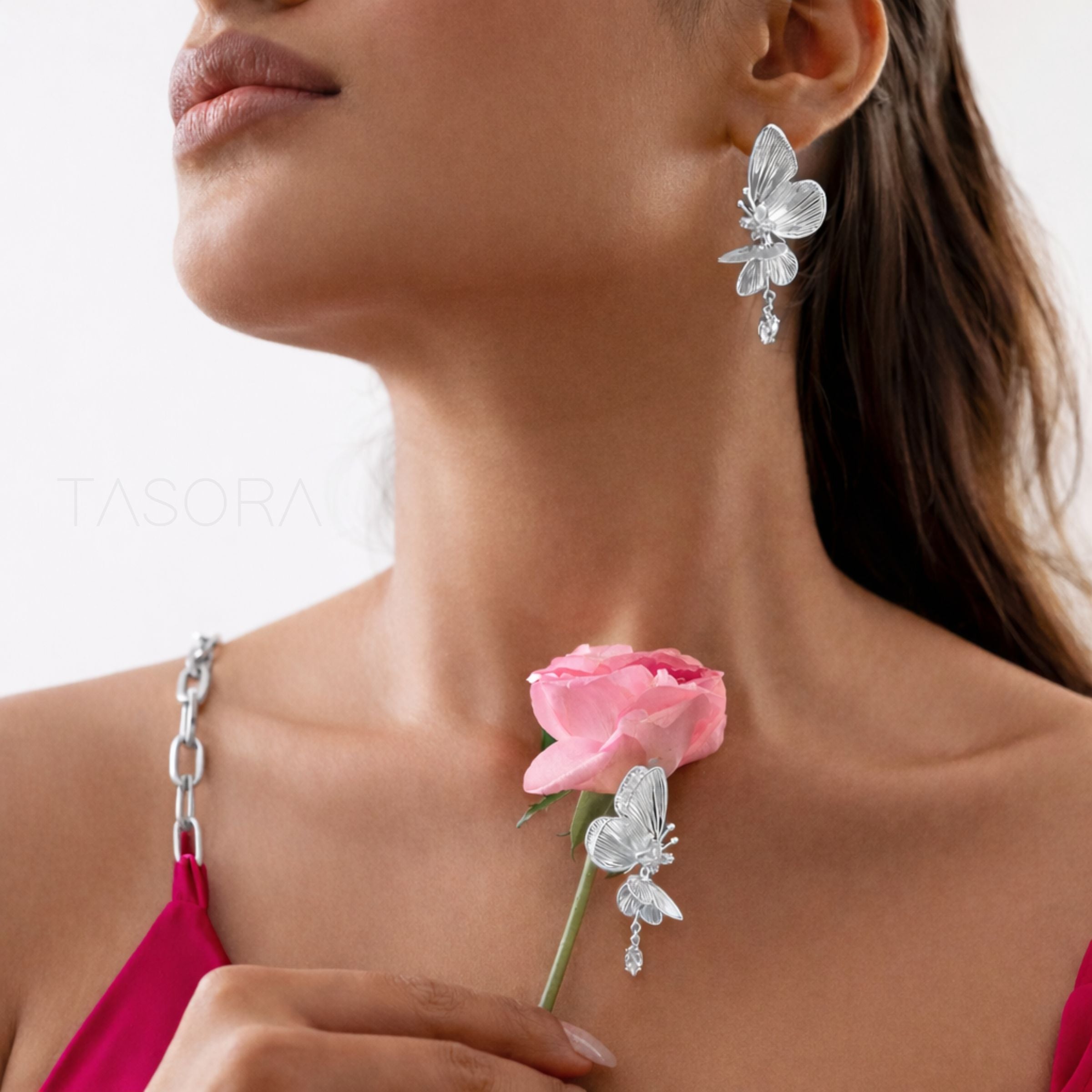 Woman wearing silver butterfly earrings with a pink rose against a neutral background