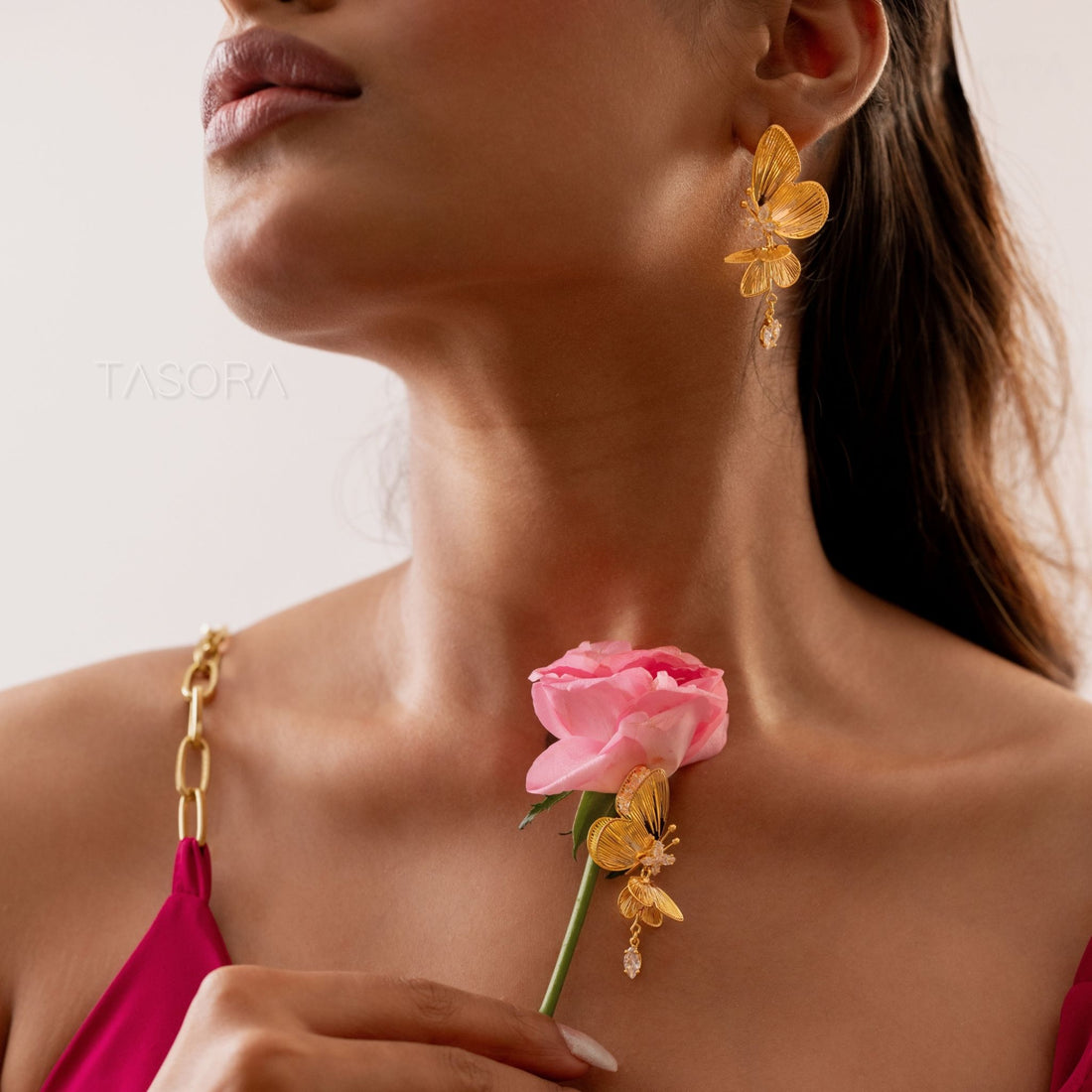 Butterfly-shaped Blinky Butterfly earrings of TASORA brand on a stone surface with small flowers.