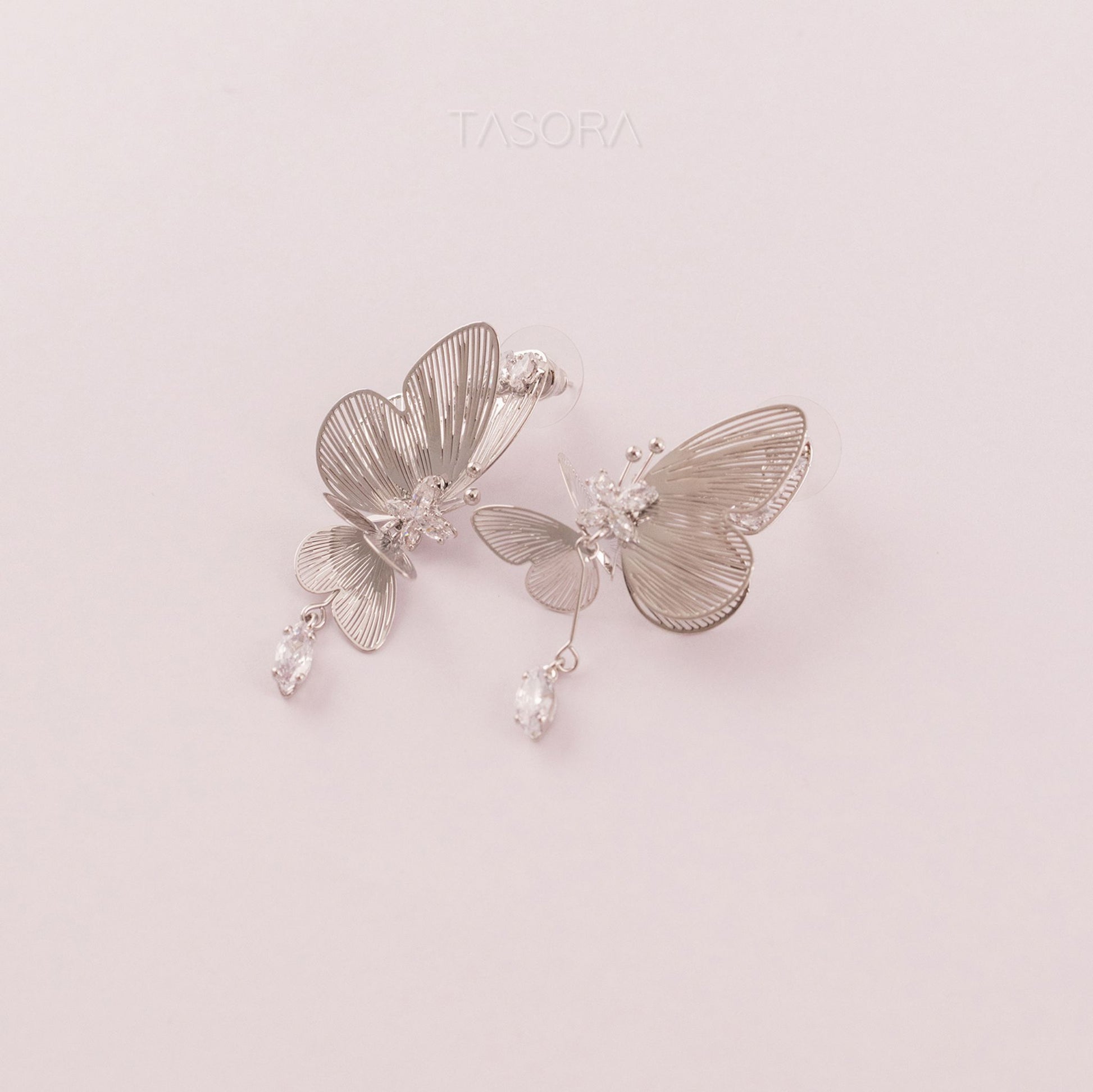 Butterfly-shaped Blinky Butterfly Silver earrings with intricate details on a light pink background with TASORA branding