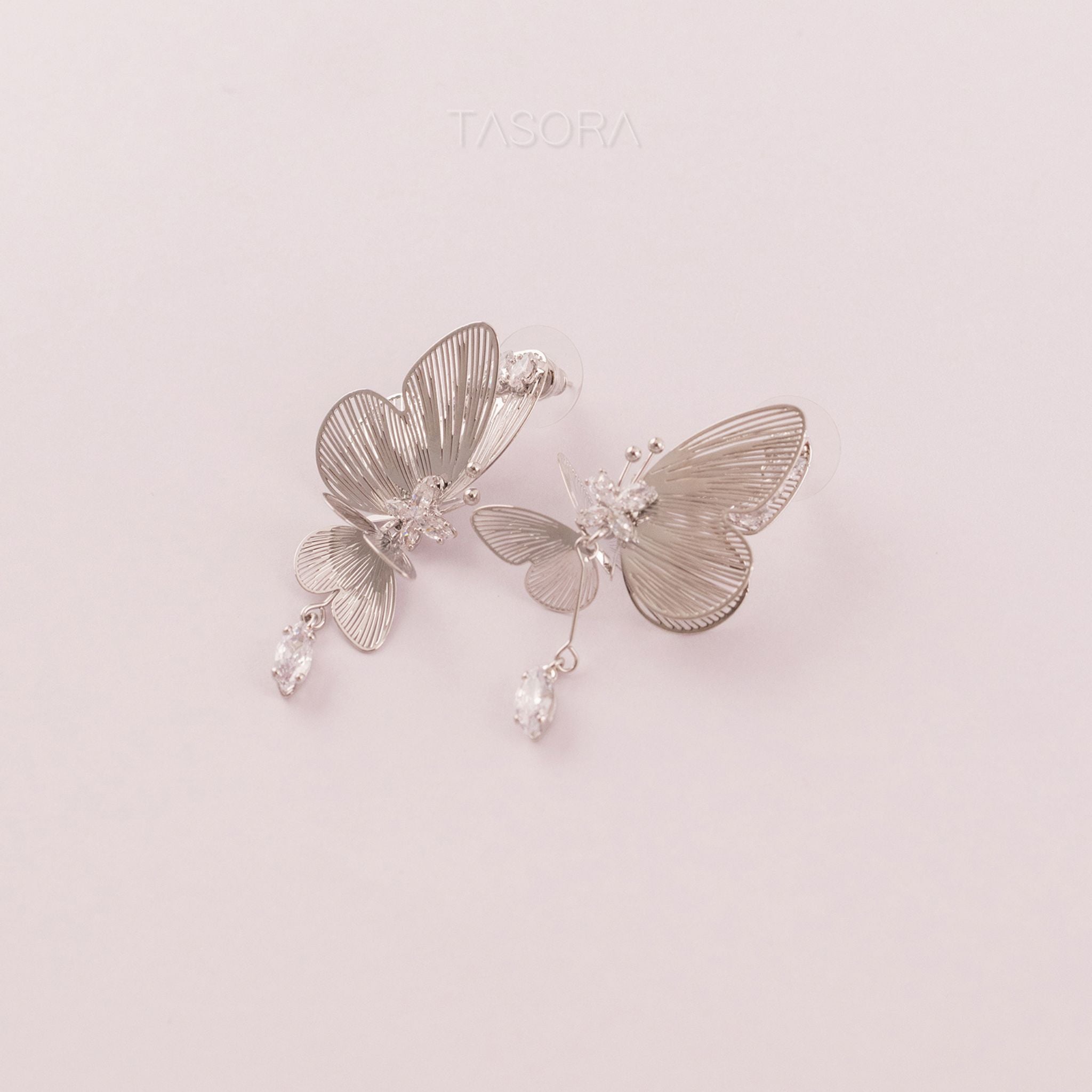 Butterfly-shaped Blinky Butterfly Silver earrings with intricate details on a light pink background with TASORA branding