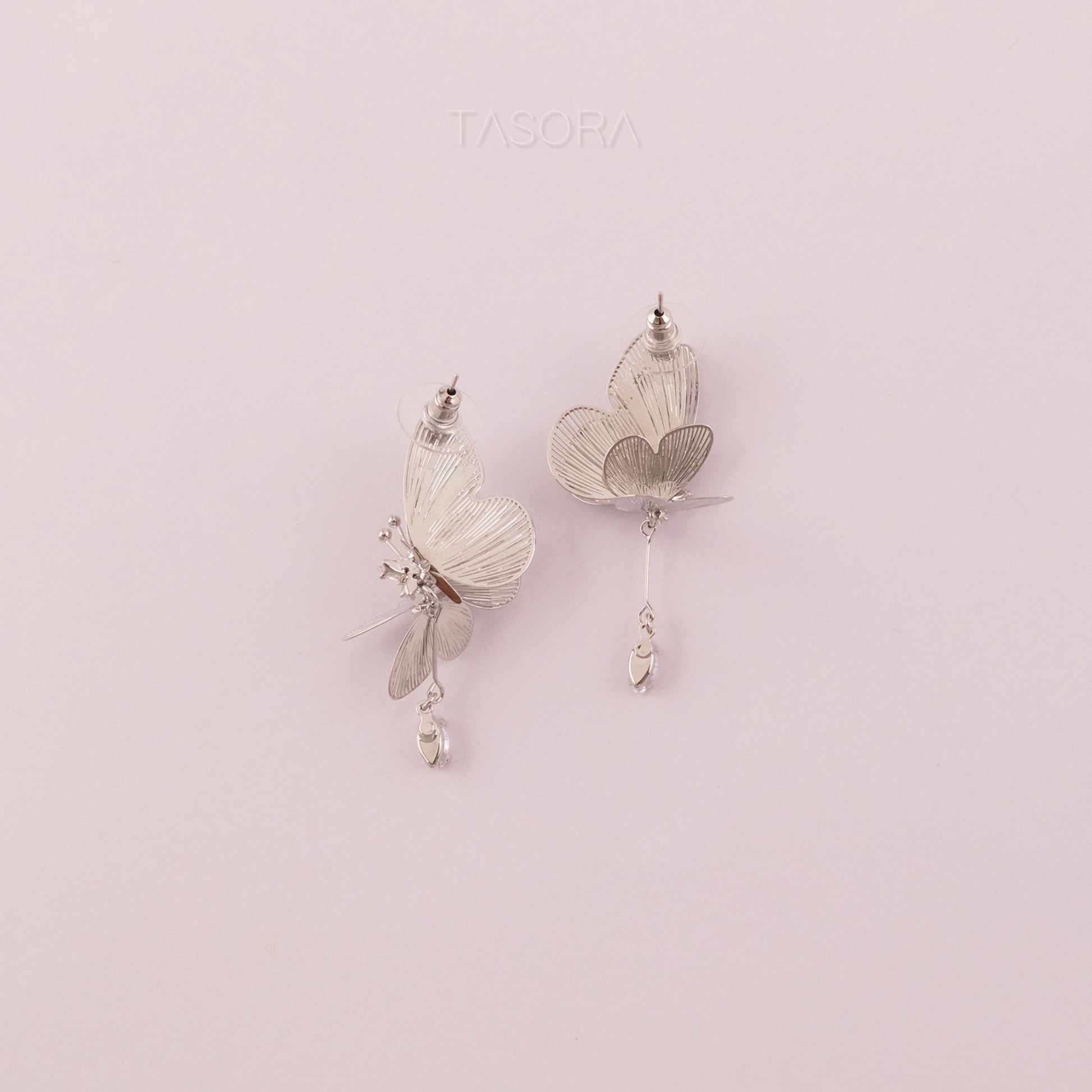 Back side of Blinky Butterfly Silver earrings on a light pink background with 'TASORA' branding.