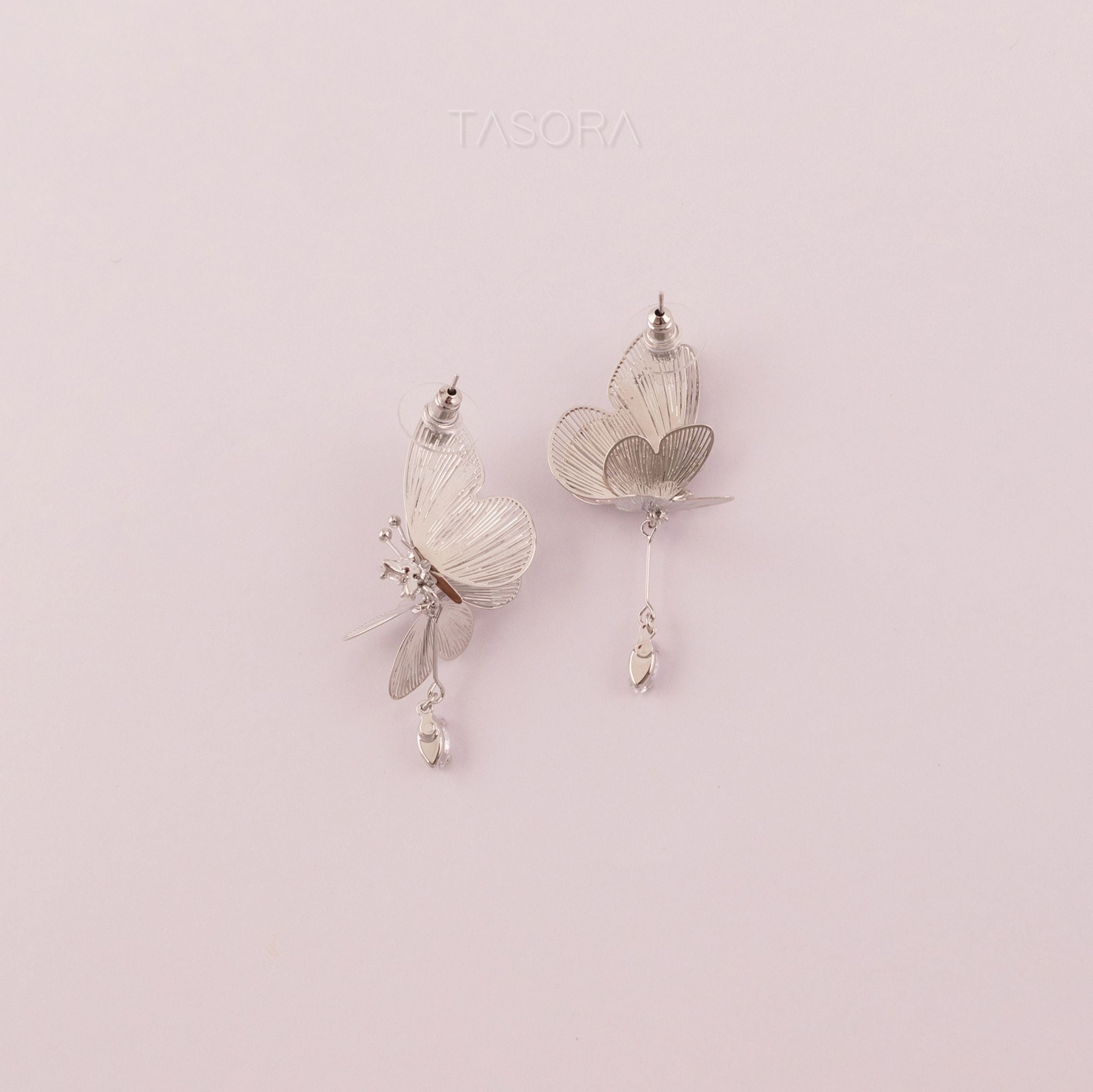 Back side of Blinky Butterfly Silver earrings on a light pink background with 'TASORA' branding.