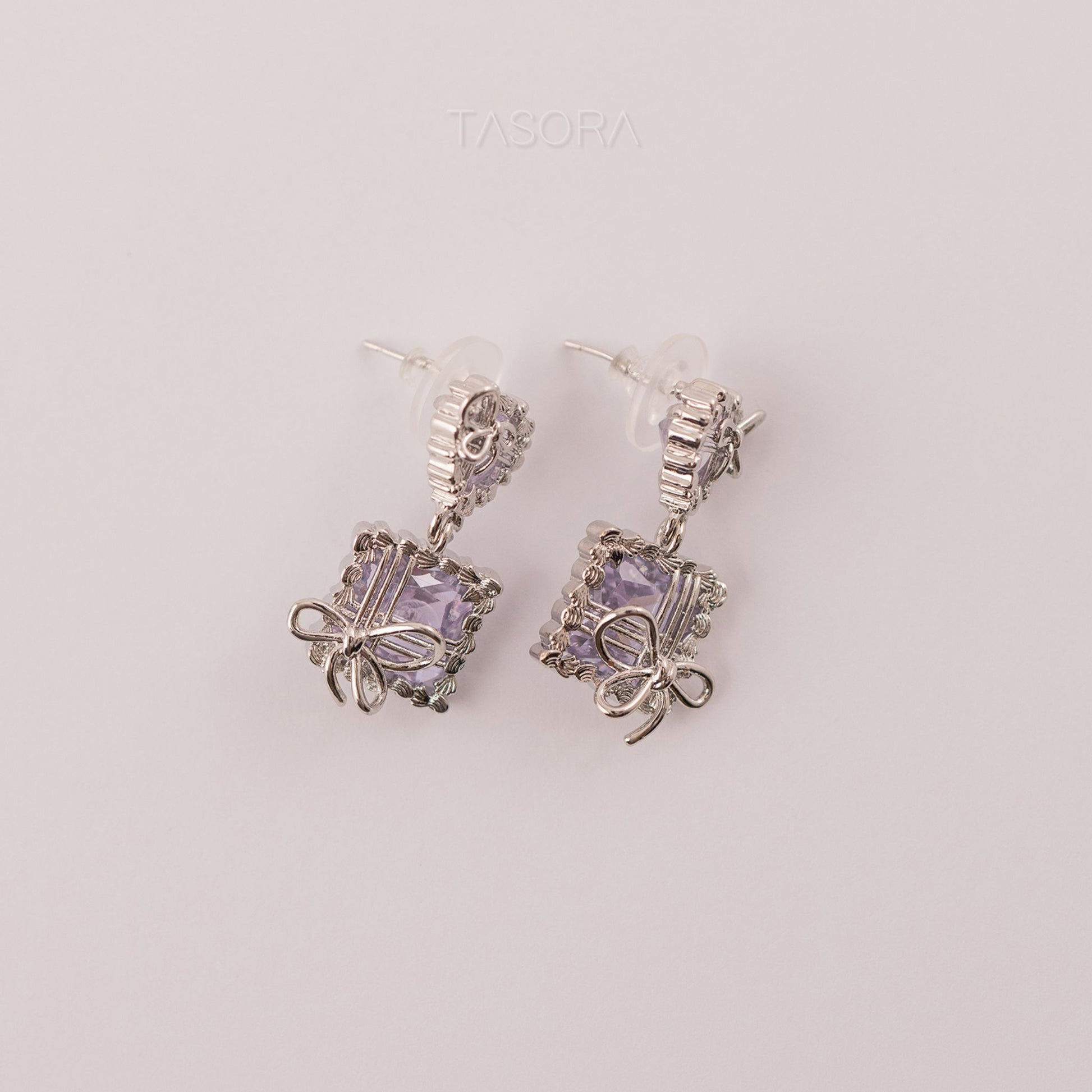 Silver Bow Belle earrings by TASORA with purple gemstones on a light gray background