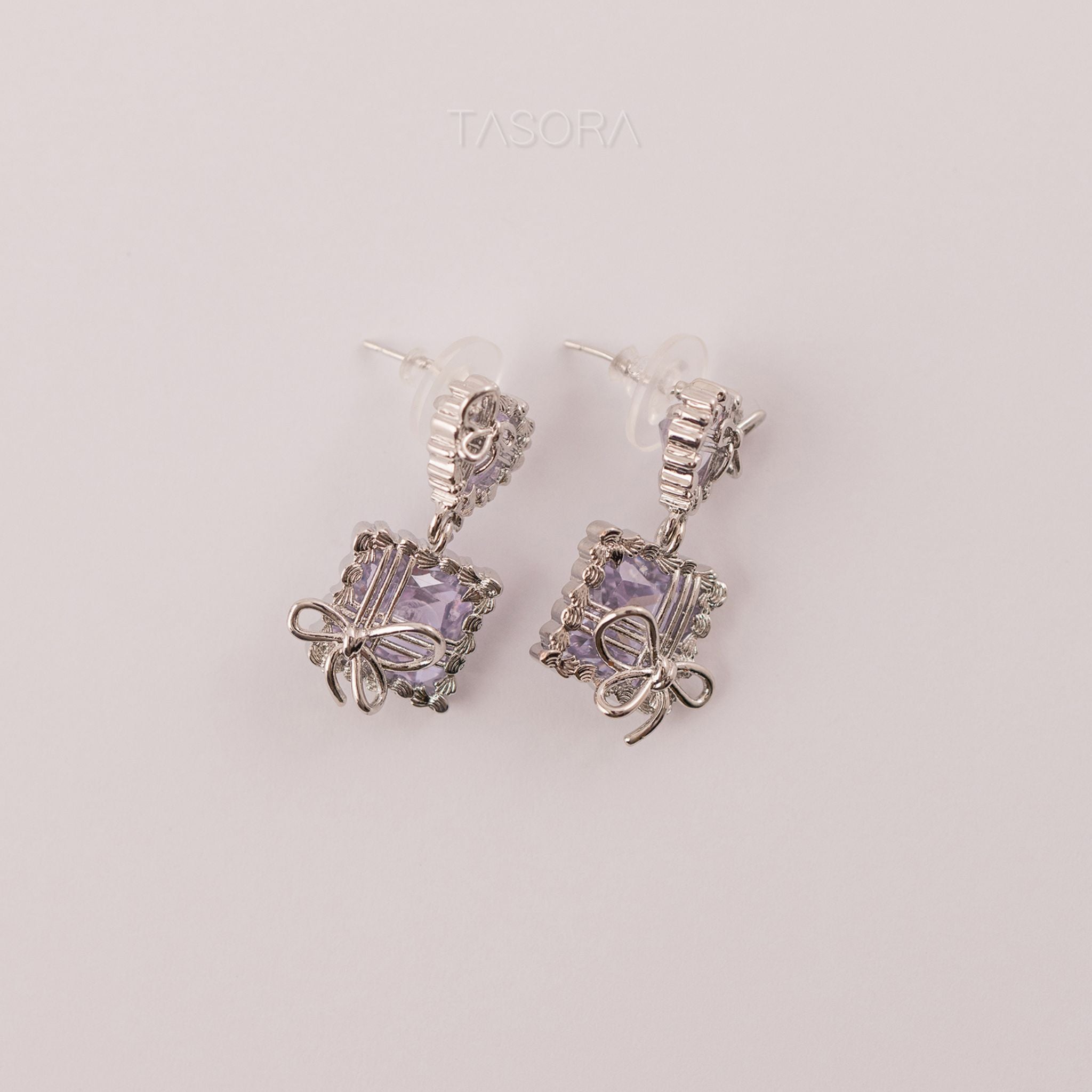 Silver Bow Belle earrings by TASORA with purple gemstones on a light gray background