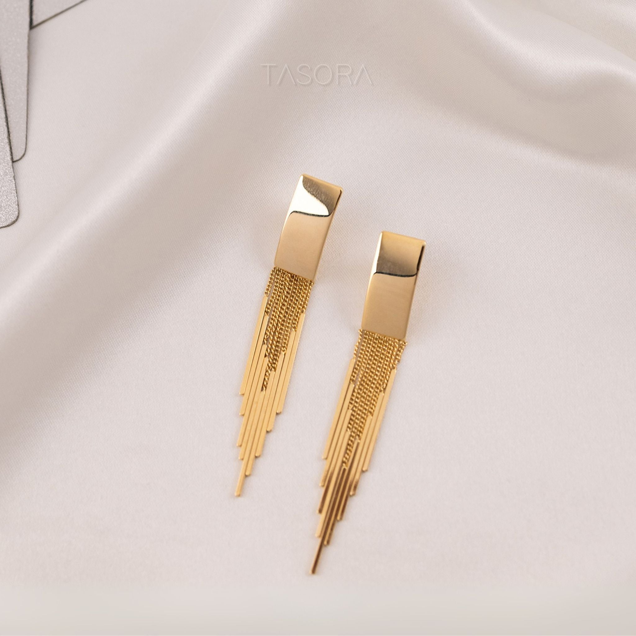 Front look of Cascade Flow golden earrings on a light fabric background with 'TASORA' branding.