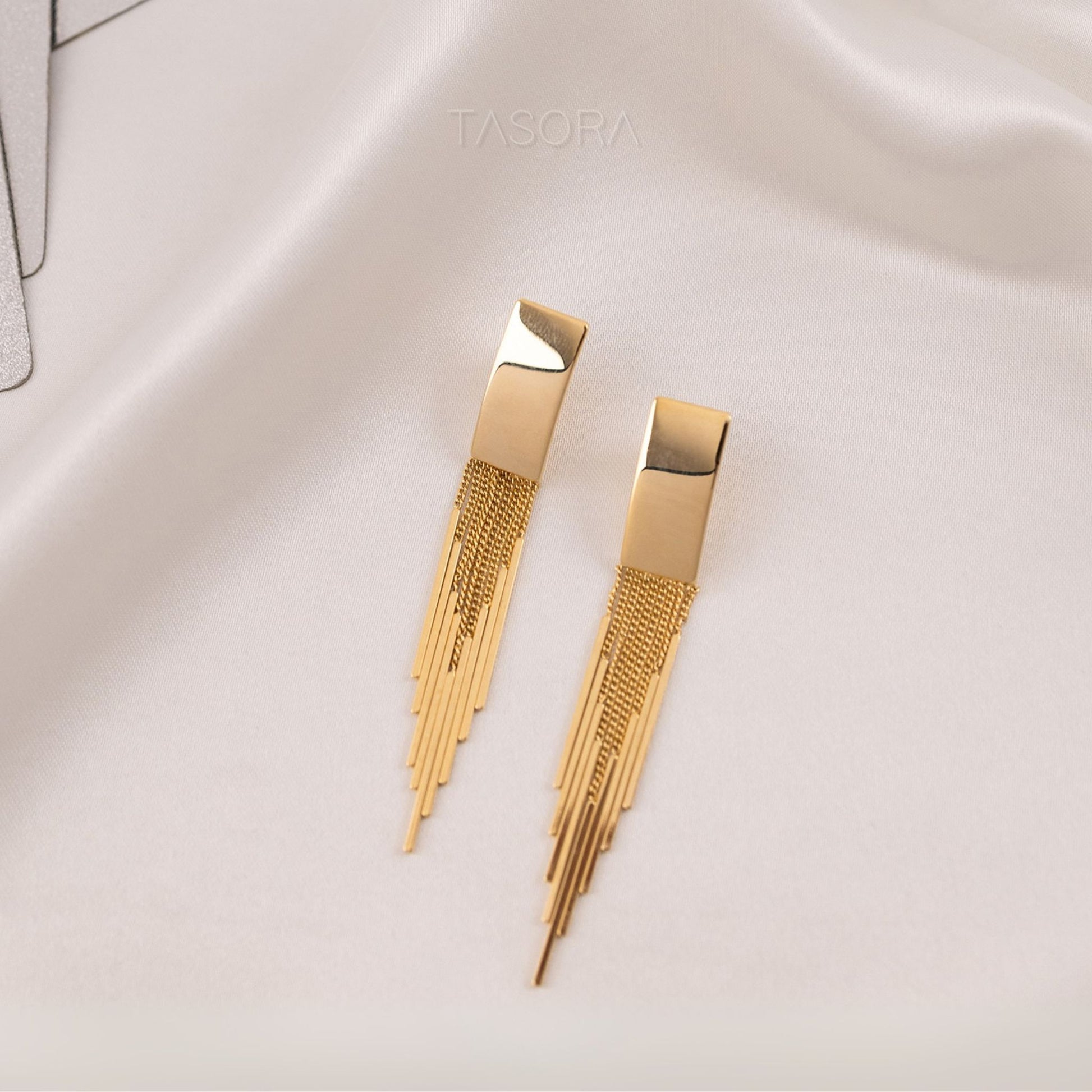 Front look of Cascade Flow golden earrings on a light fabric background with 'TASORA' branding.