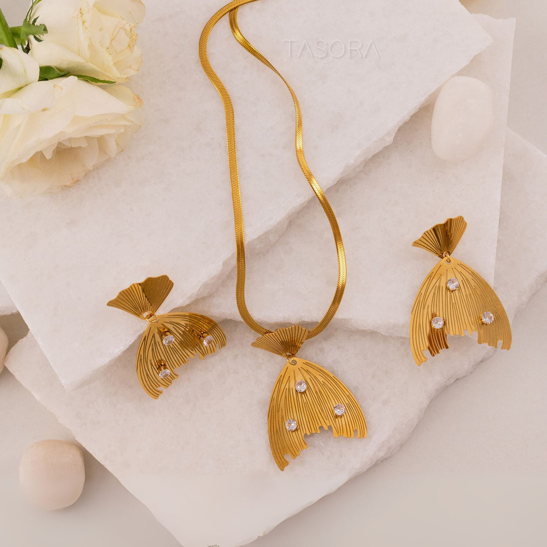 Golden Cascade Gleam necklace and earrings by TASORA on a white stone surface with flowers