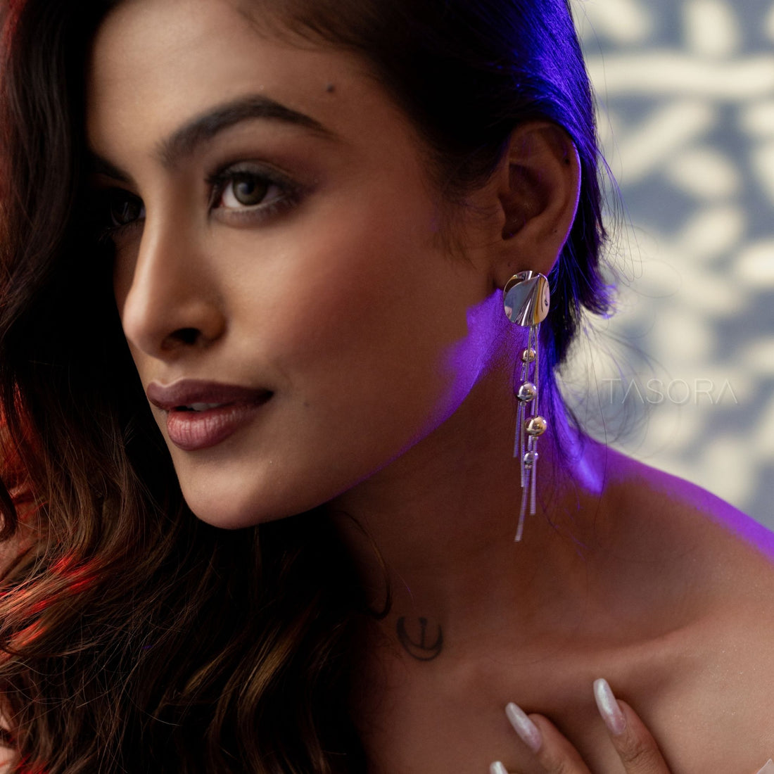 Glass with Disco Drizzle earrings by TASORA, placed on a textured surface with a plant in the background