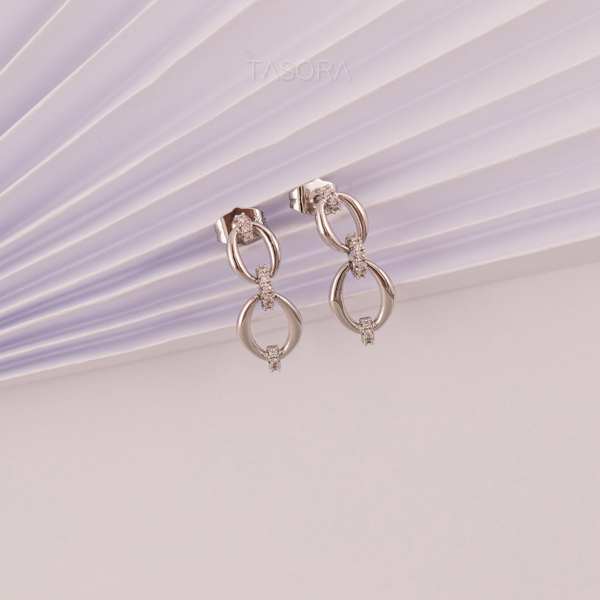 Pair of Elior silver earrings on a light purple and white striped background with 'TASORA' branding.