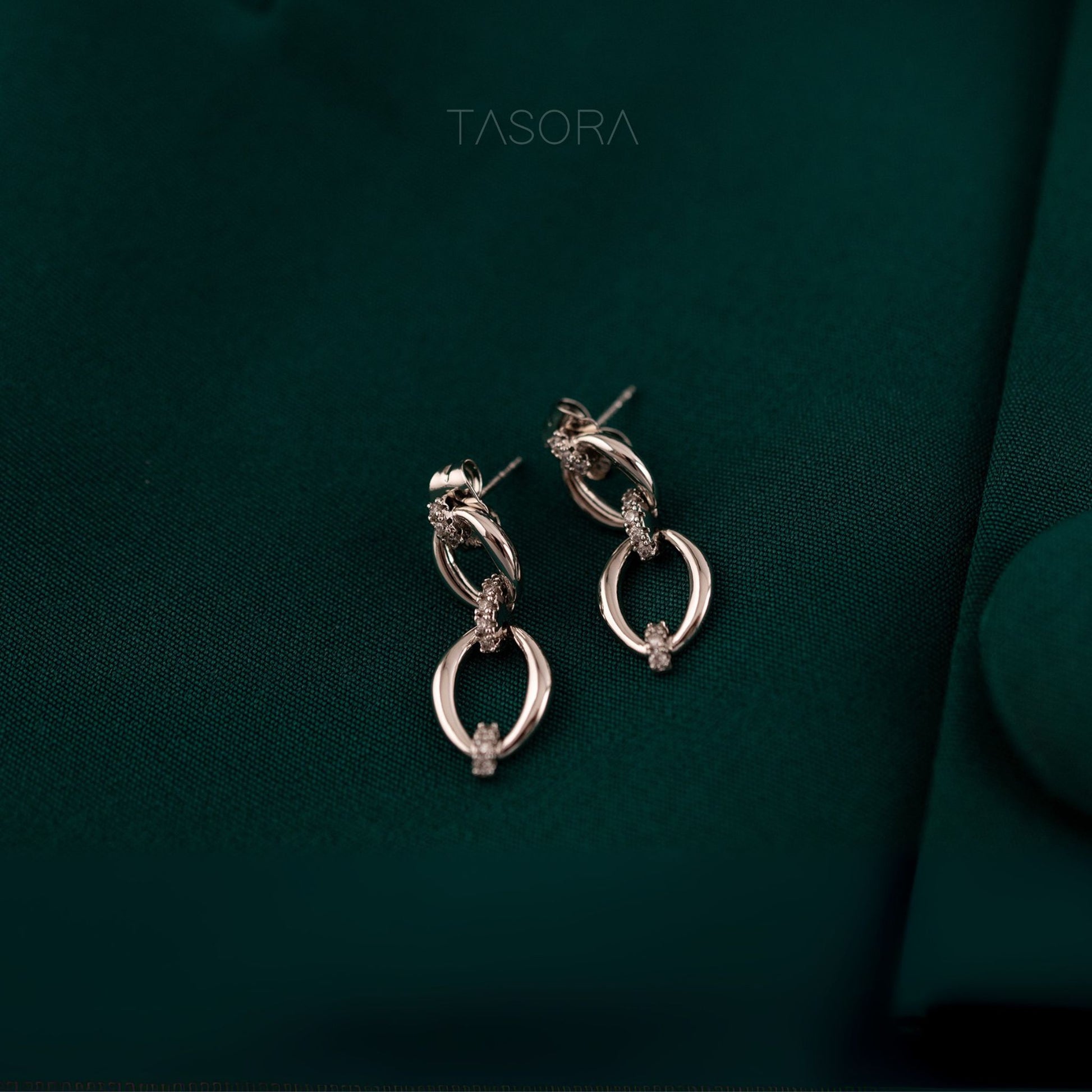 Elior Silver earrings on a dark green fabric background with 'TASORA' branding.