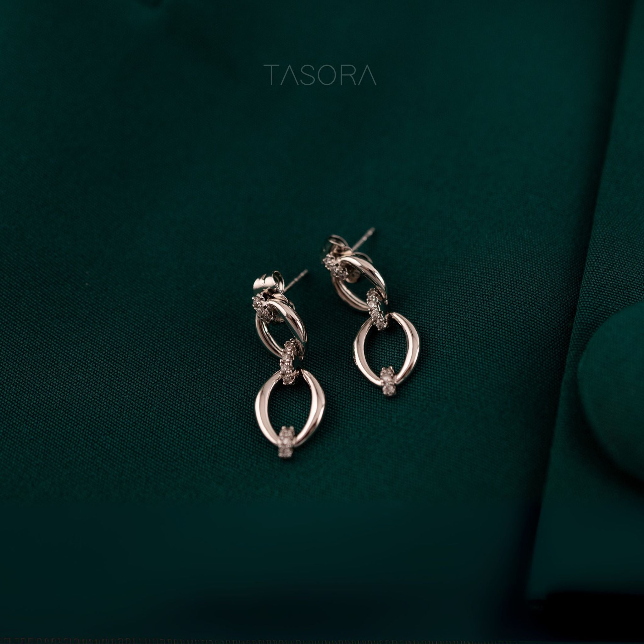 Elior Silver earrings on a dark green fabric background with 'TASORA' branding.