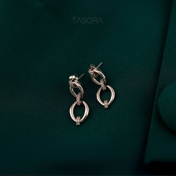 Elior Silver earrings on a dark green fabric background with 'TASORA' branding.