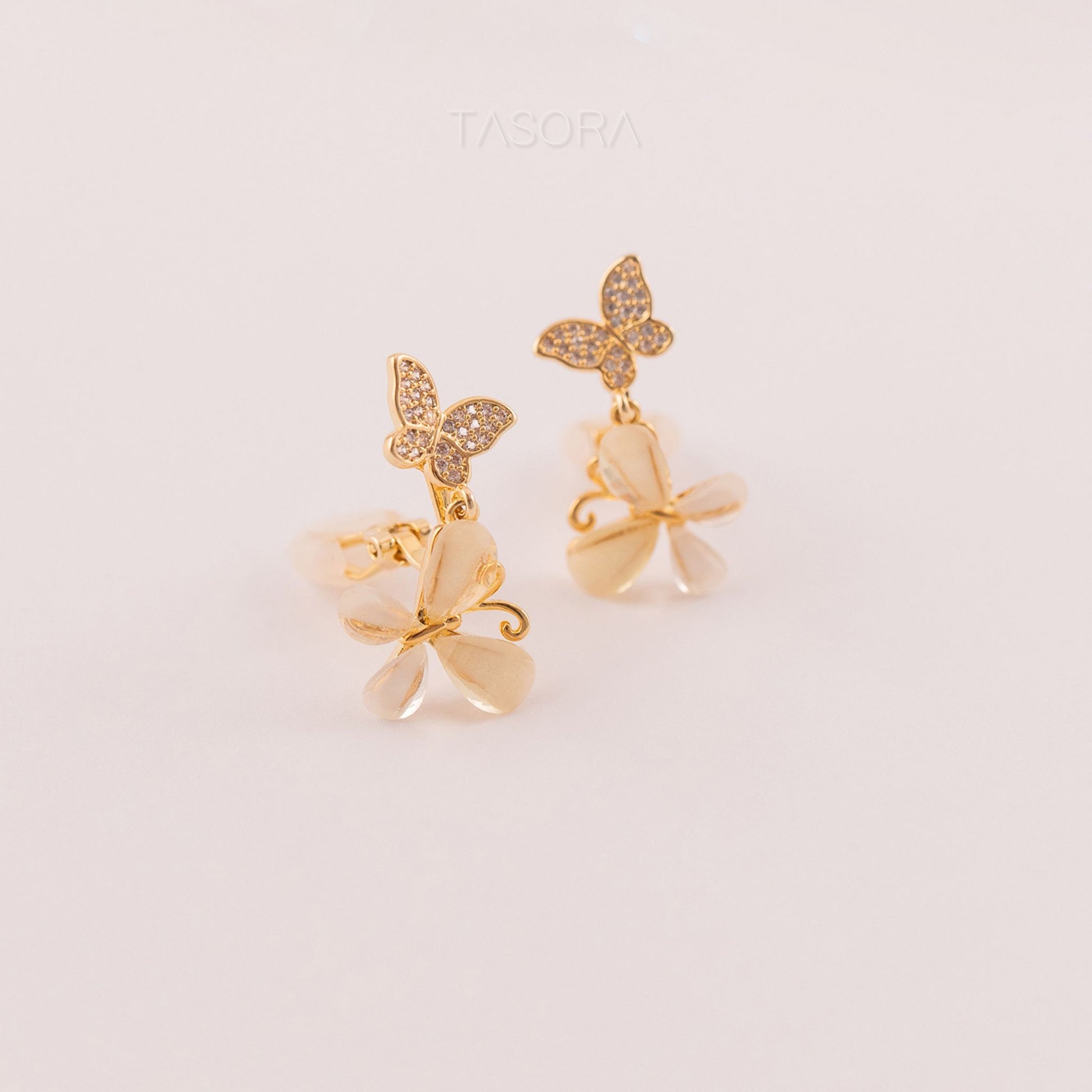 Butterfly-shaped Flutter Petal earrings with gold accents on a light beige background, featuring the brand 'TASORA'.