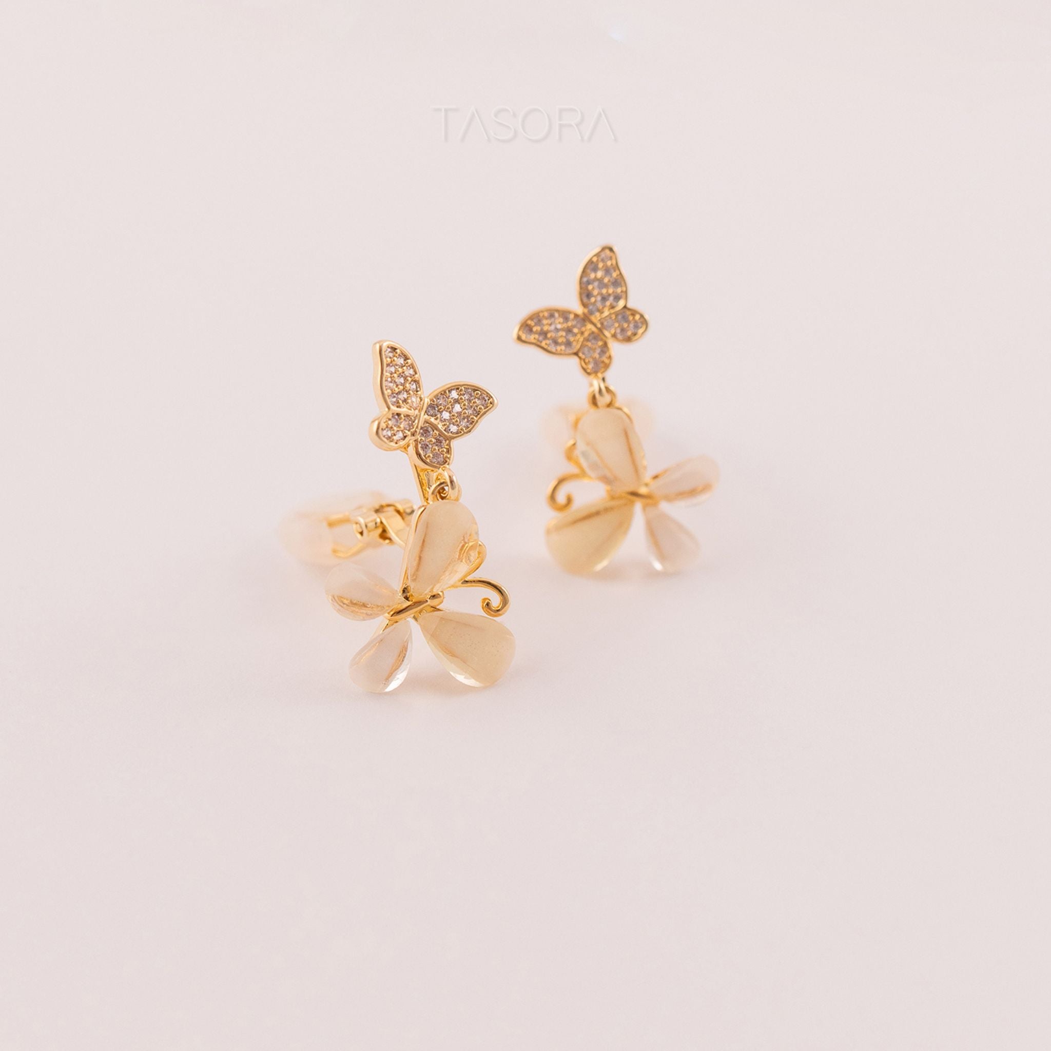 Butterfly-shaped Flutter Petal earrings with gold accents on a light beige background, featuring the brand 'TASORA'.