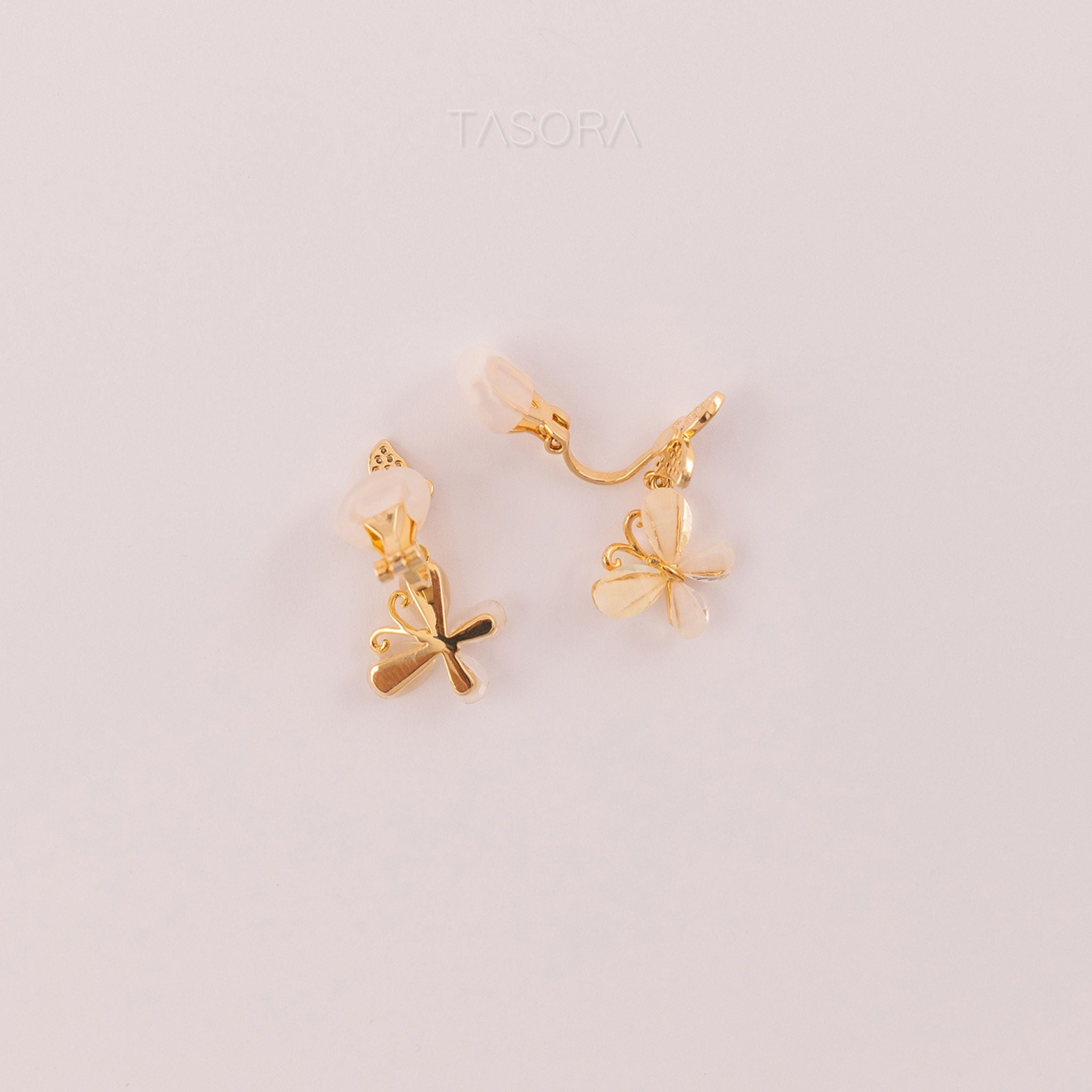 Side look of golden Flutter Petal earrings on a light pink background with 'TASORA' branding.