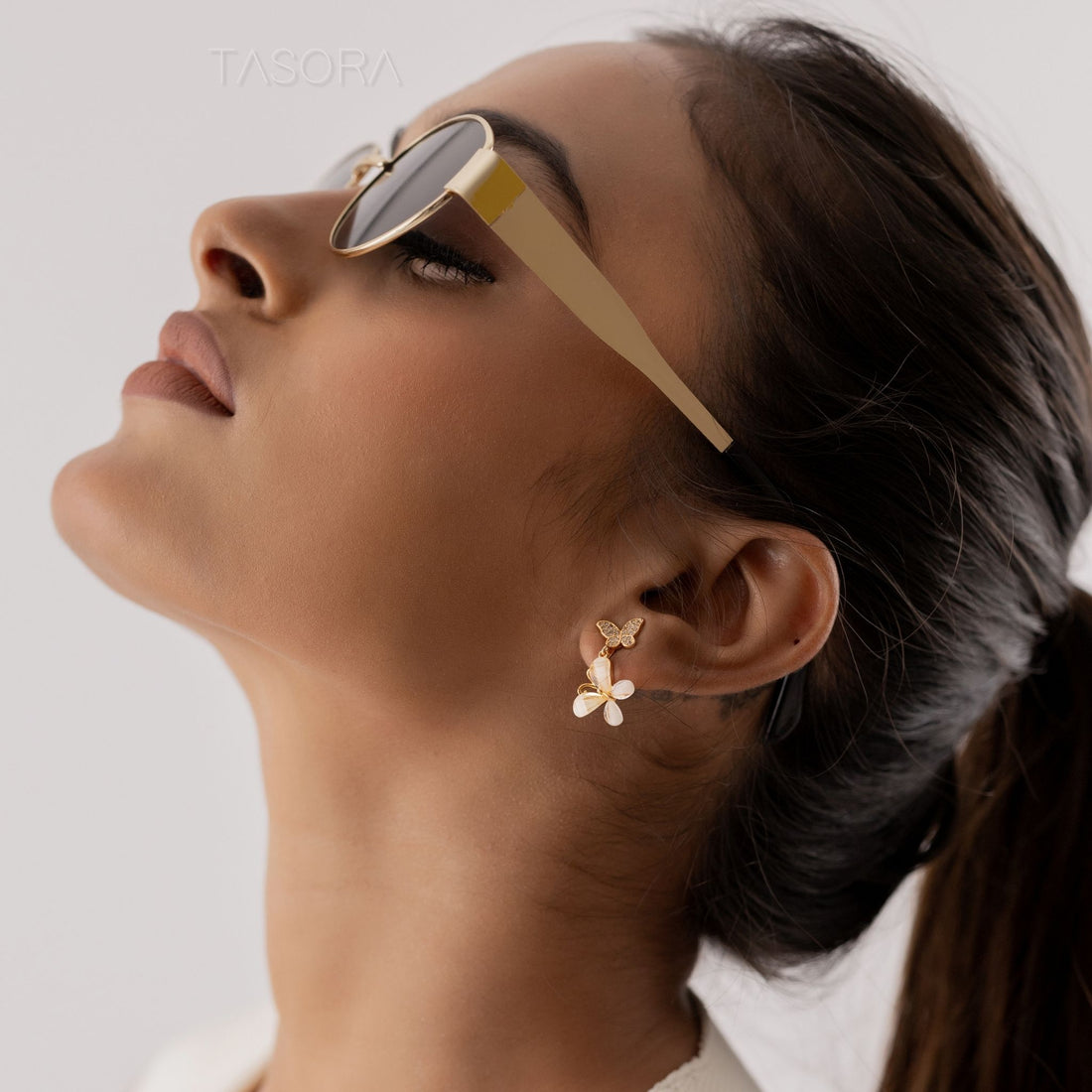 Golden Flutter Petal earrings on a branch with a phone in the background, branded 'TASORA'.