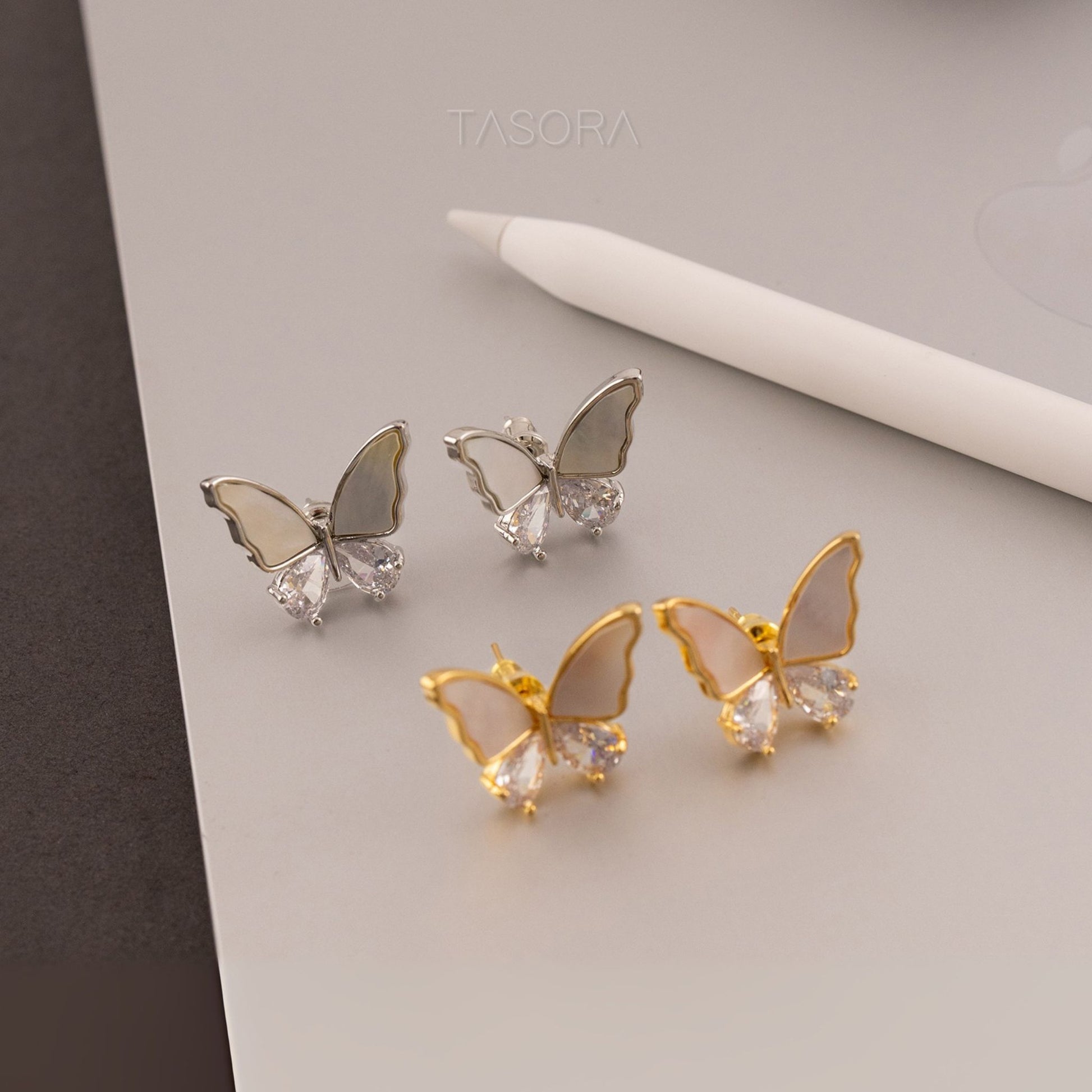 Butterfly-shaped Flutter wings earrings in gold and silver on a light gray background with 'TASORA' branding.