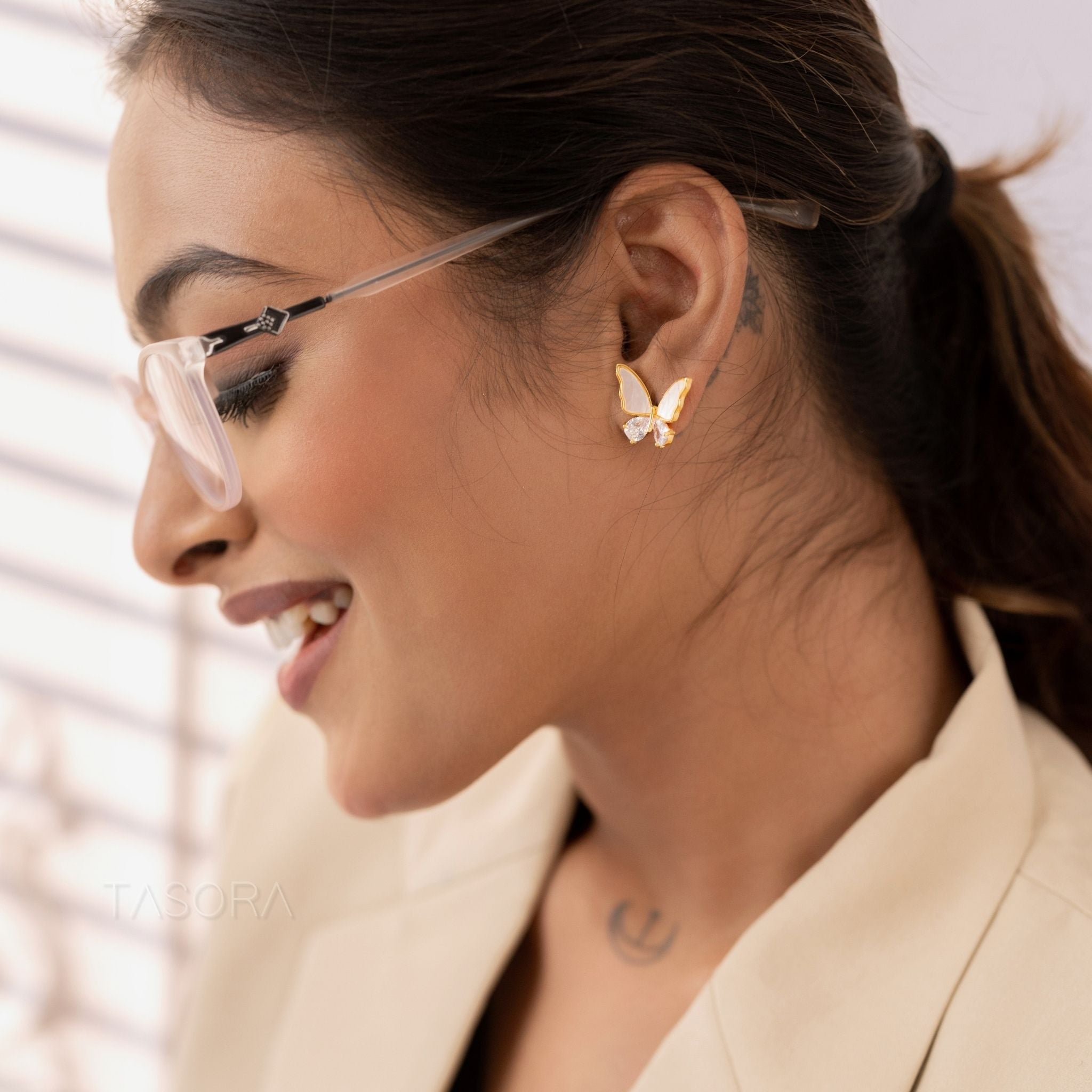 Woman wearing butterfly shaped Flutter wings earrings of TASORA brand with a neutral background