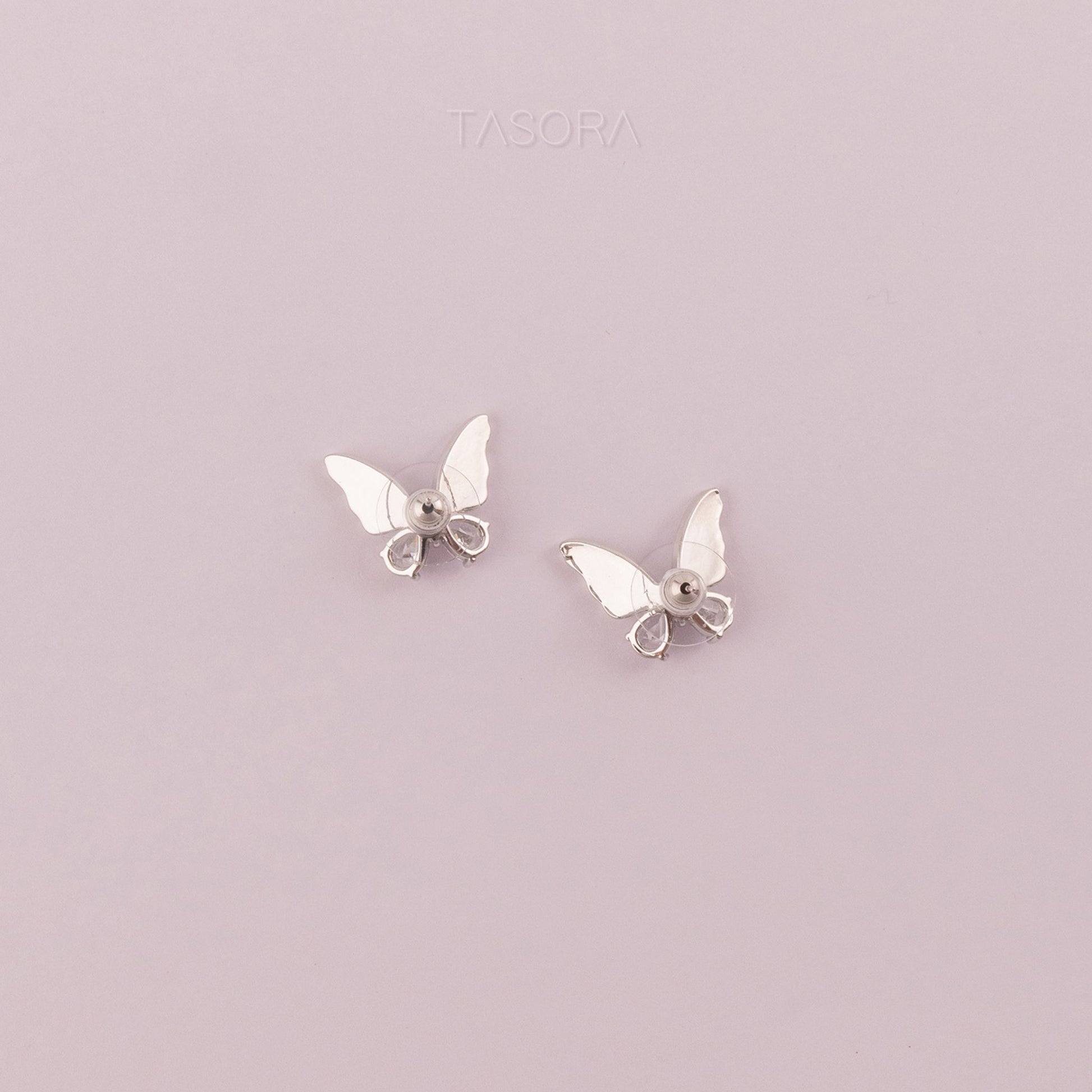 Back side of Butterfly-shaped Flutter wings silver earrings on a light purple background with 'TASORA' branding.
