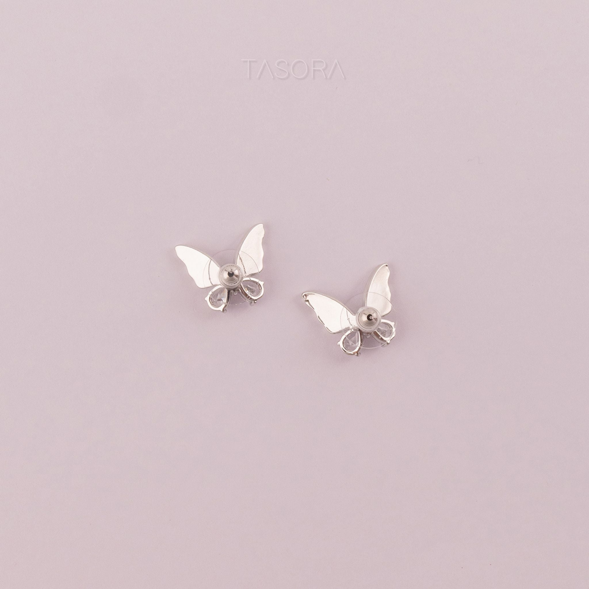 Back side of Butterfly-shaped Flutter wings silver earrings on a light purple background with 'TASORA' branding.