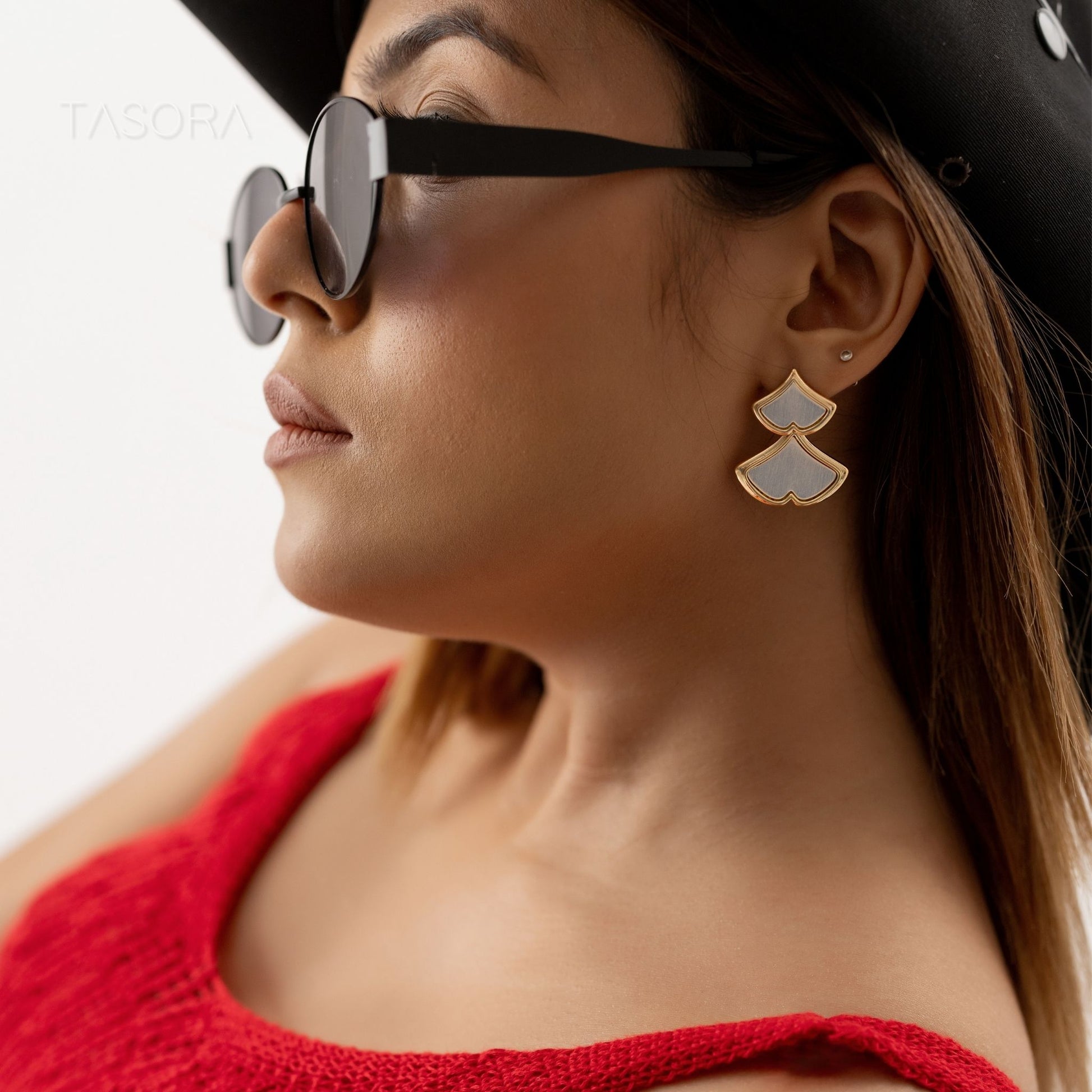 Woman wearing sunglasses and TASORA brand Golden Glint earrings with a red top, close-up of face.