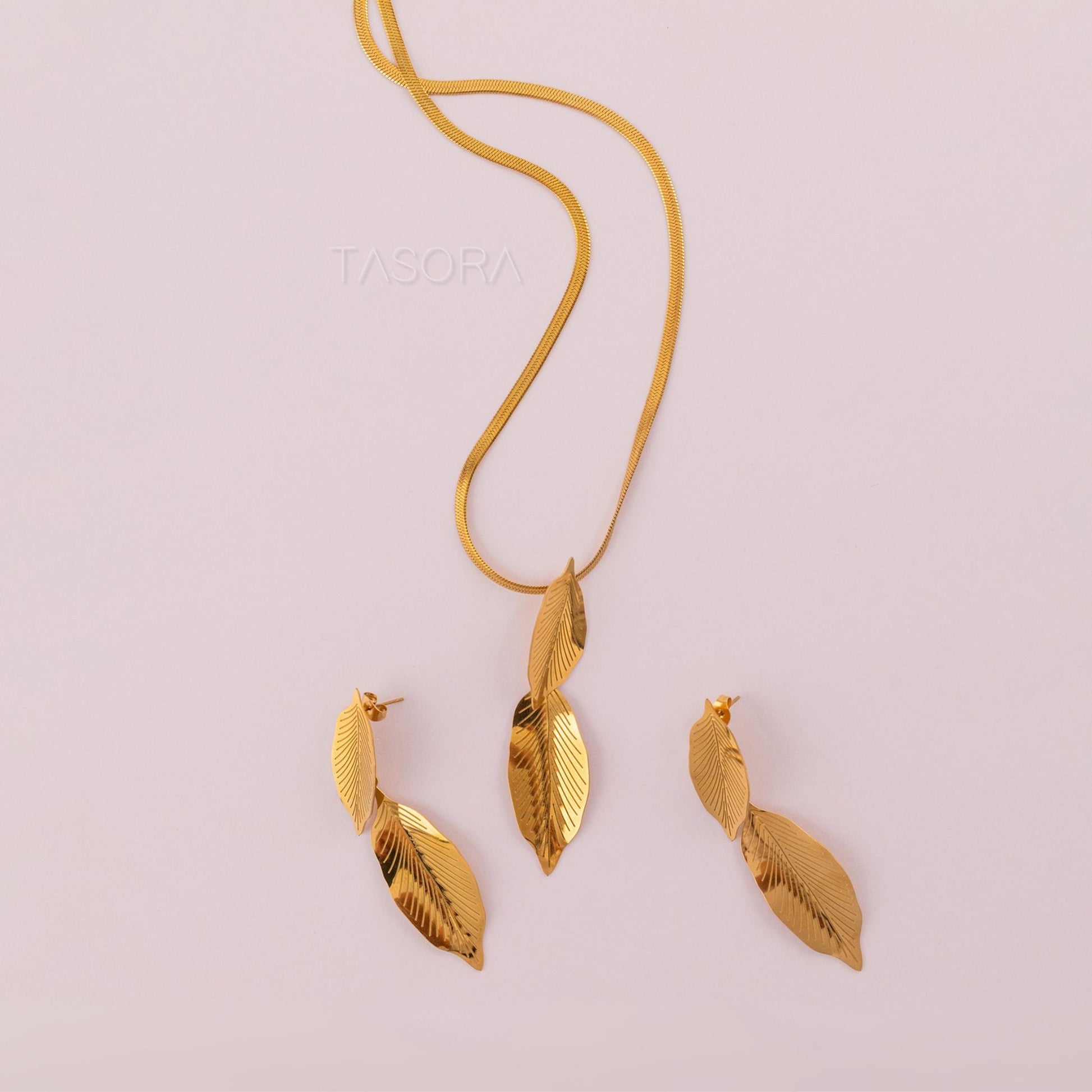 Gold leaf shape Lustre Leaf necklace and earrings on a light pink background with 'TASORA' branding.