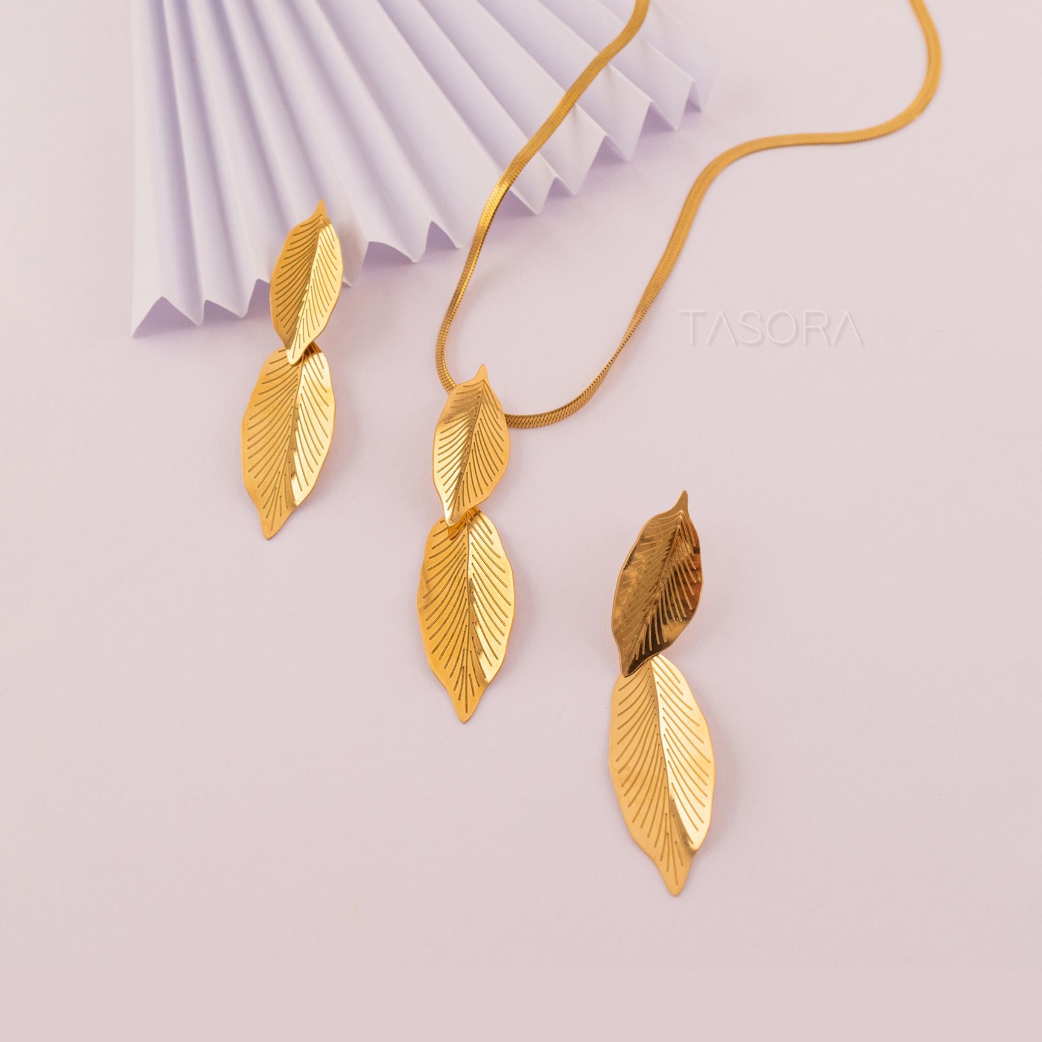 Gold leaf-shaped Lustre Leaf necklace on a light pink background with 'TASORA' branding.