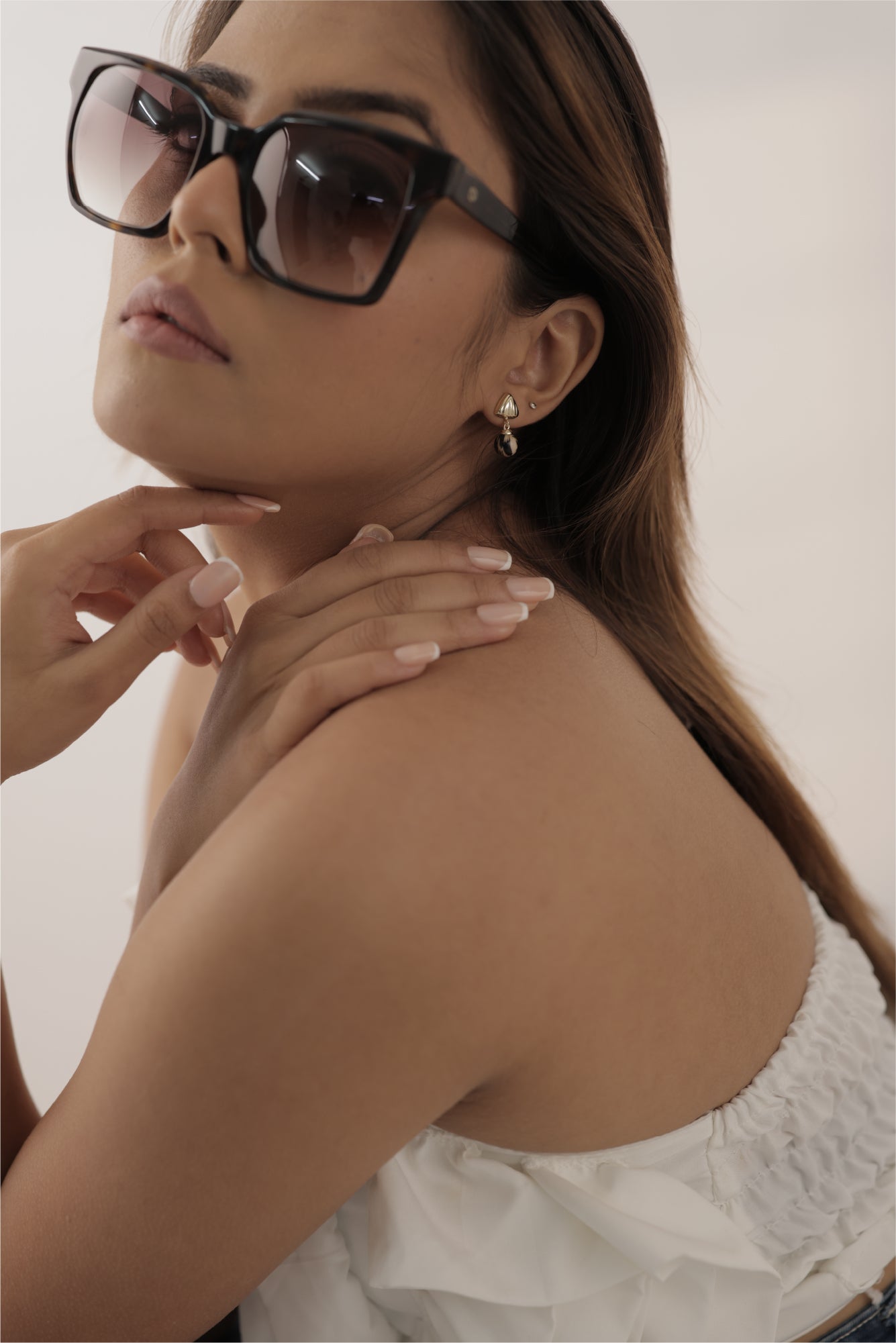 Woman wearing sunglasses and TASORA earrings with a neutral background