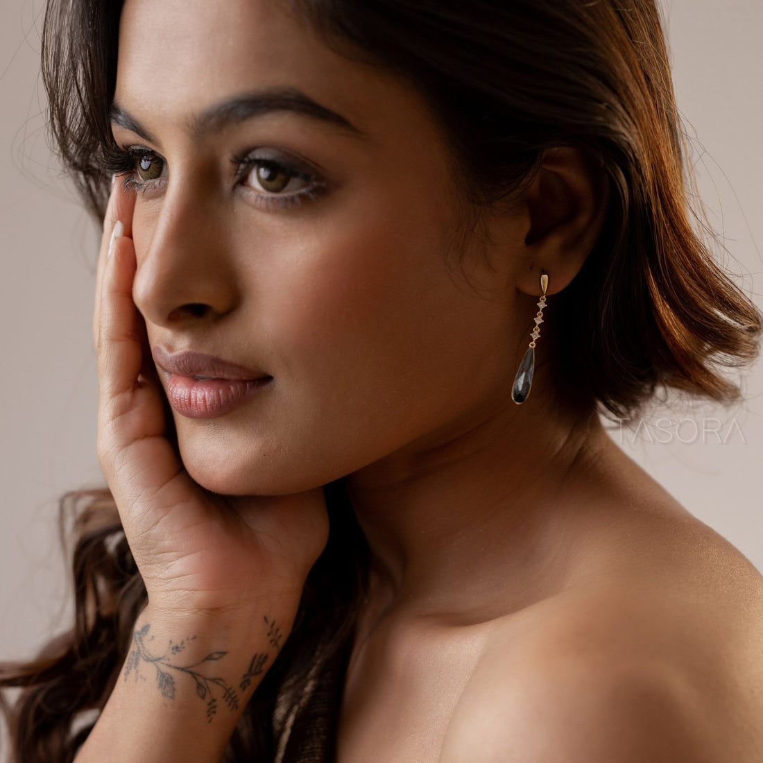 Pair of Noor Drop golden earrings with green and black teardrop-shaped stones on a clear stand with TASORA branding