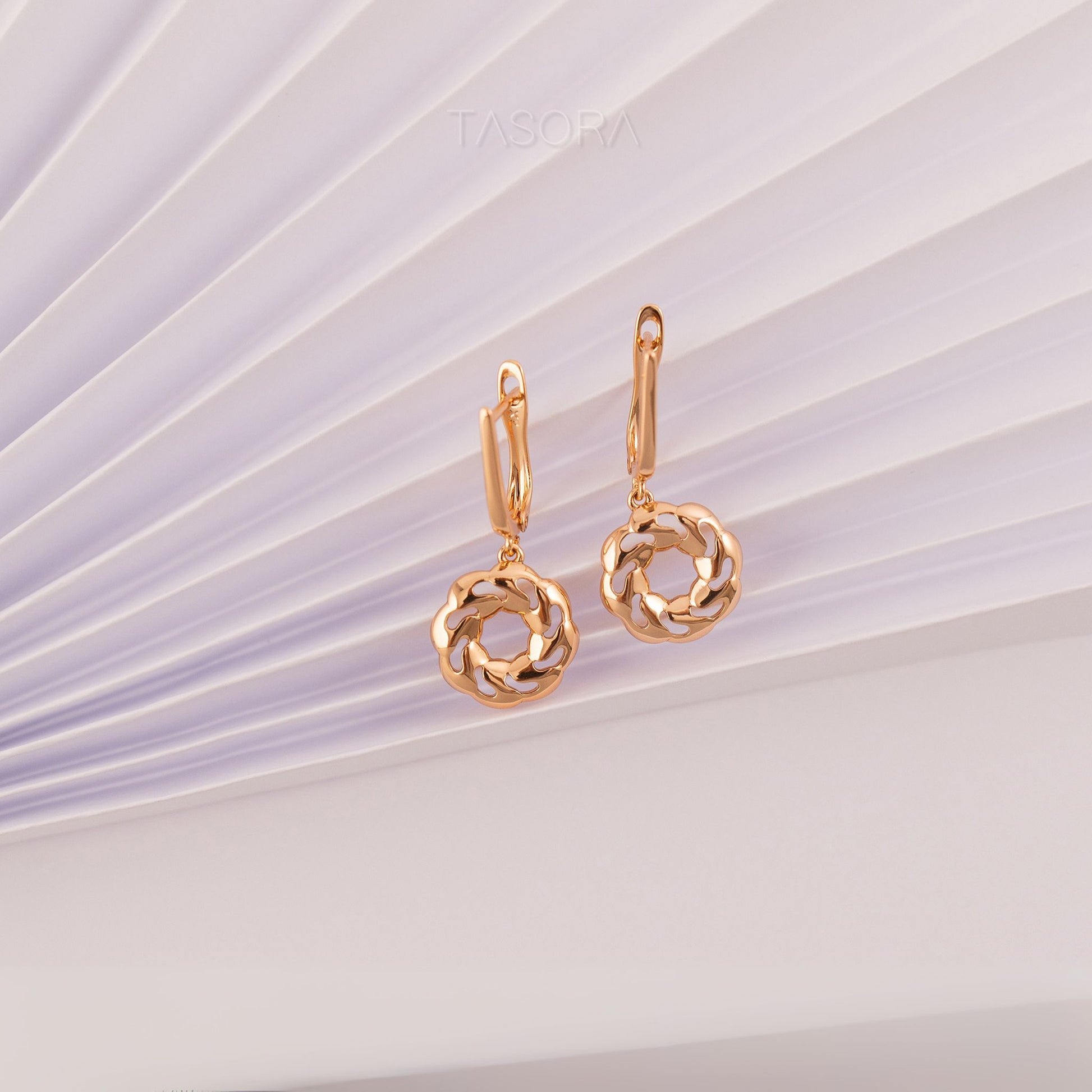 Pair of Orbbit Bloom golden earrings on a textured white and purple background with 'TASORA' branding