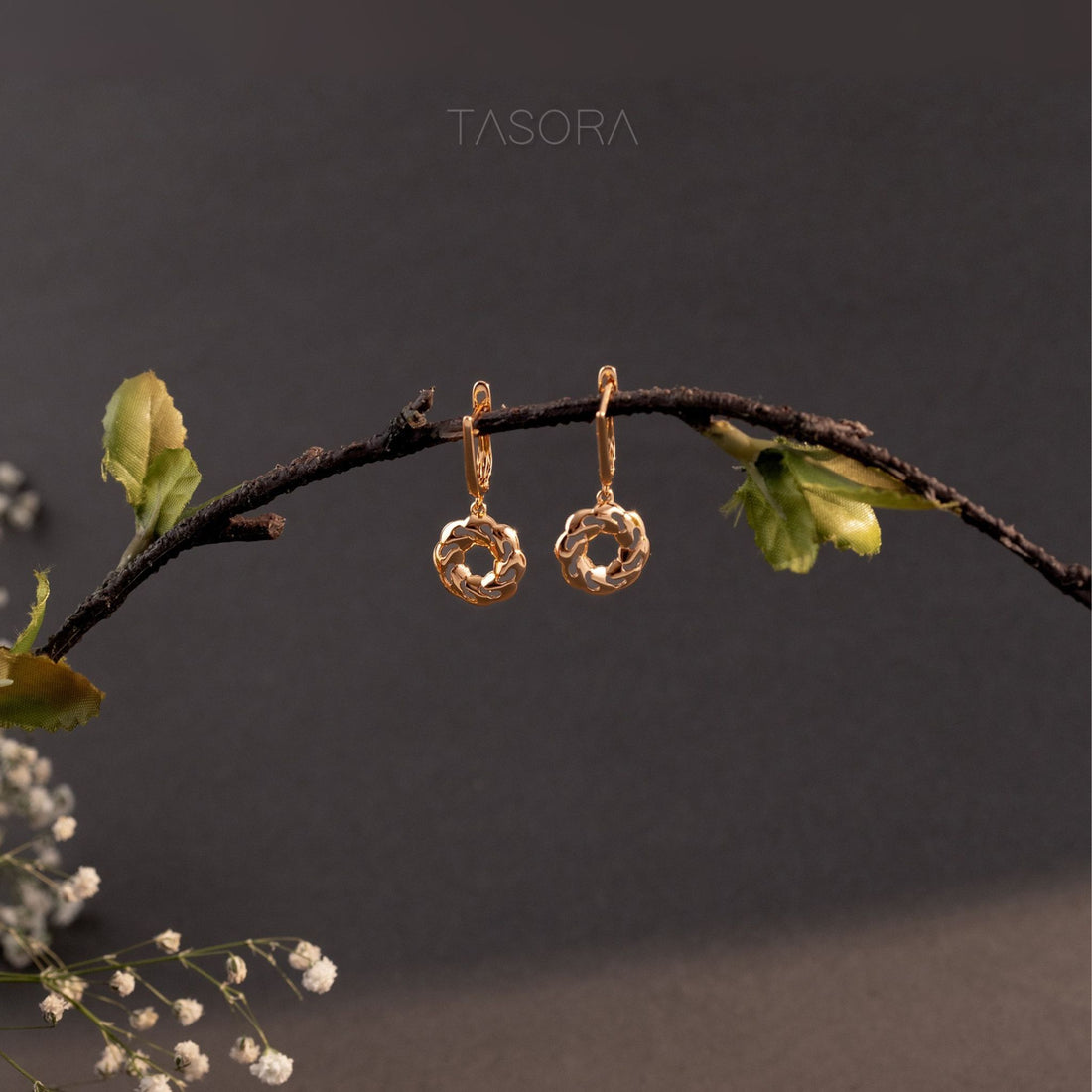 Orbbit Bloom Golden earrings hanging on a branch with a dark background with 'TASORA' branding