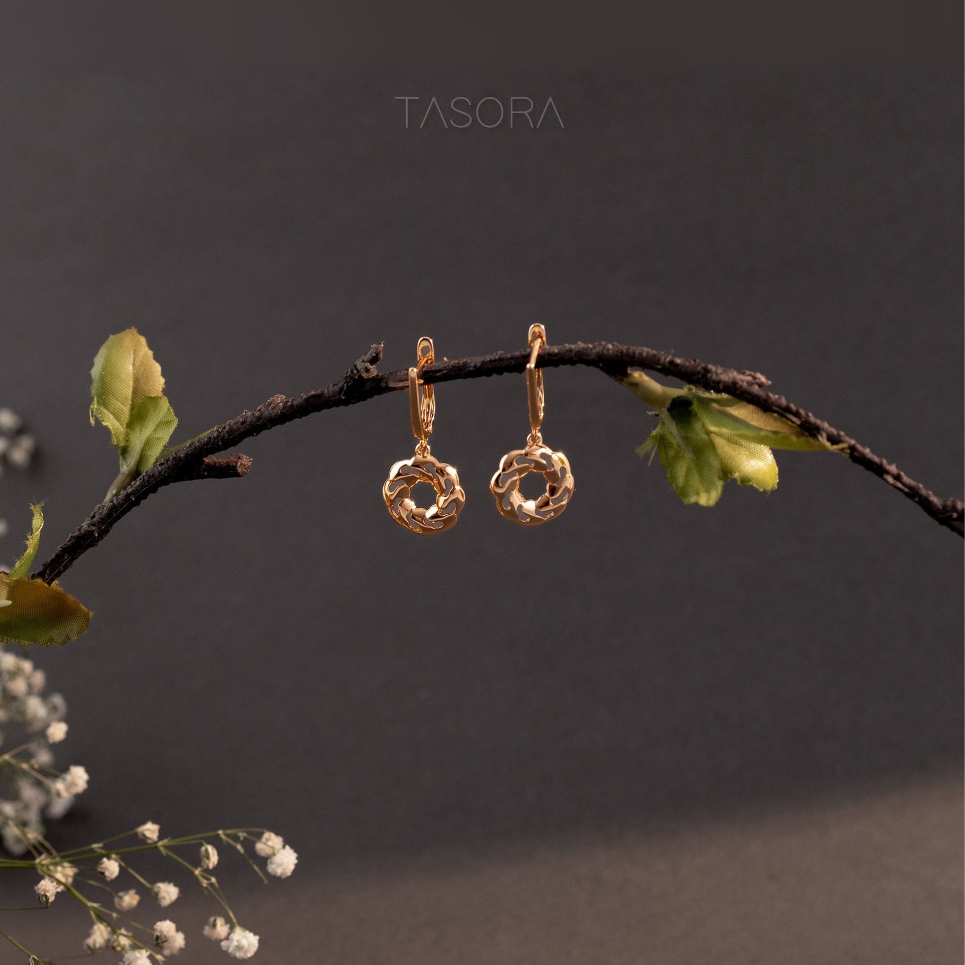 Orbbit Bloom Golden earrings hanging on a branch with a dark background with 'TASORA' branding