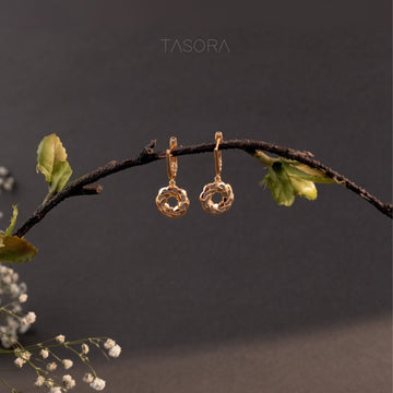 Orbbit Bloom Golden earrings hanging on a branch with a dark background with 'TASORA' branding