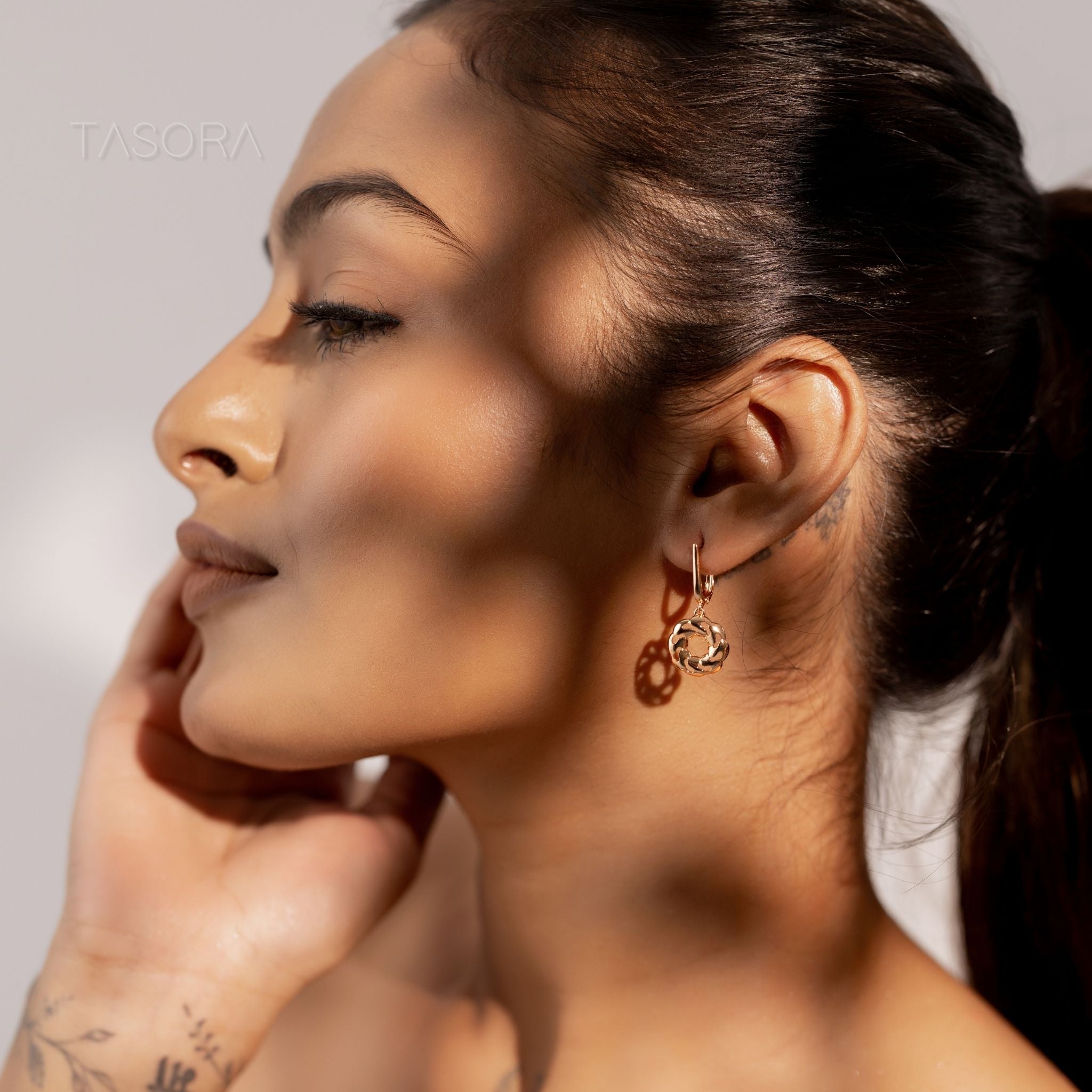 Close-up of a woman wearing TASORA brand  Orbbit Bloom golden earrings with a neutral background