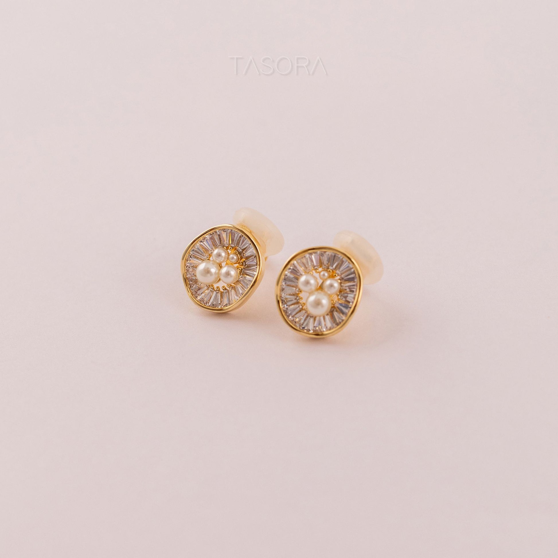 Pair of Oyster Muse Golden earrings of TASORA brand with pearl center on a light pink background