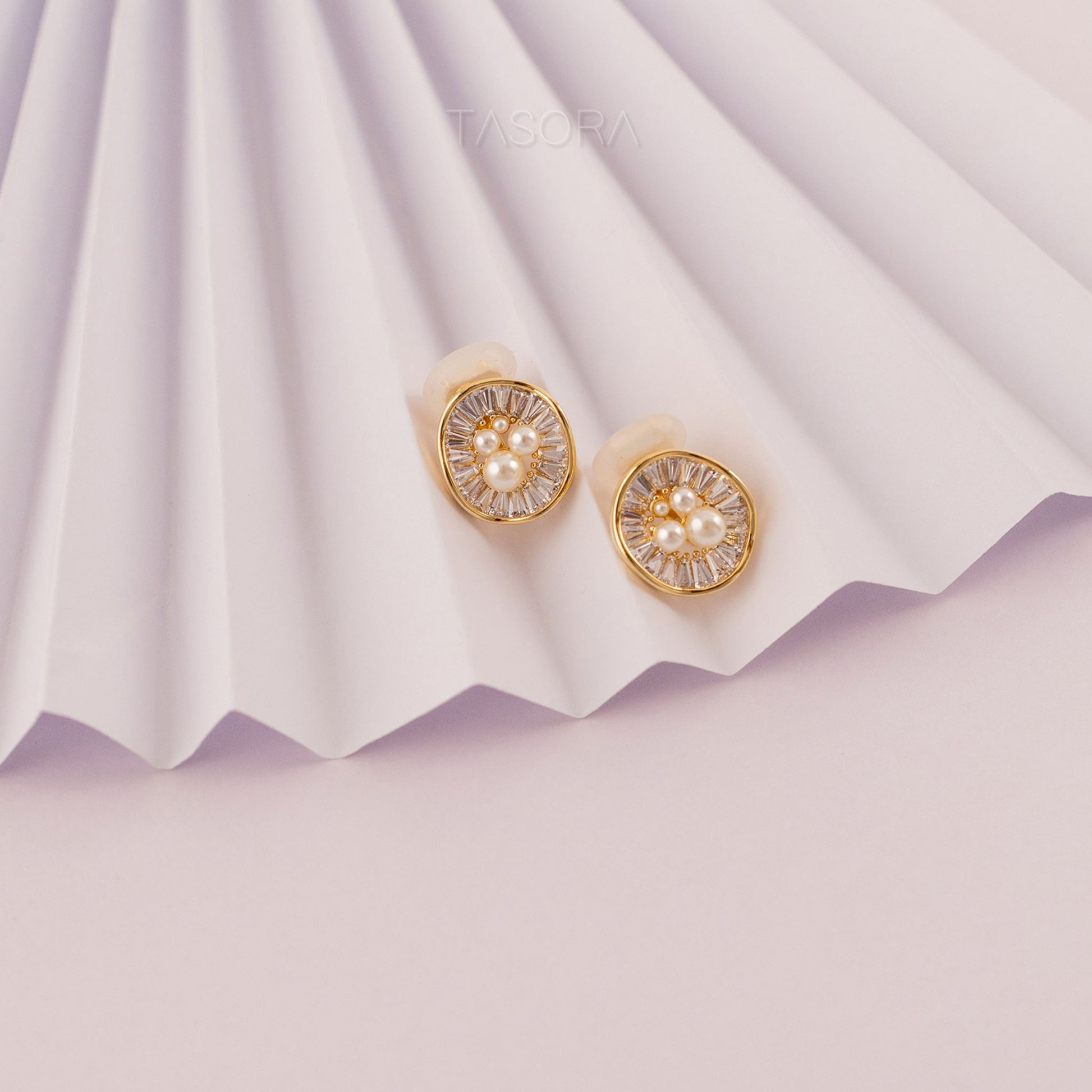 Oyster Muse Golden earrings with pearl on a white pleated paper background with TASORA branding