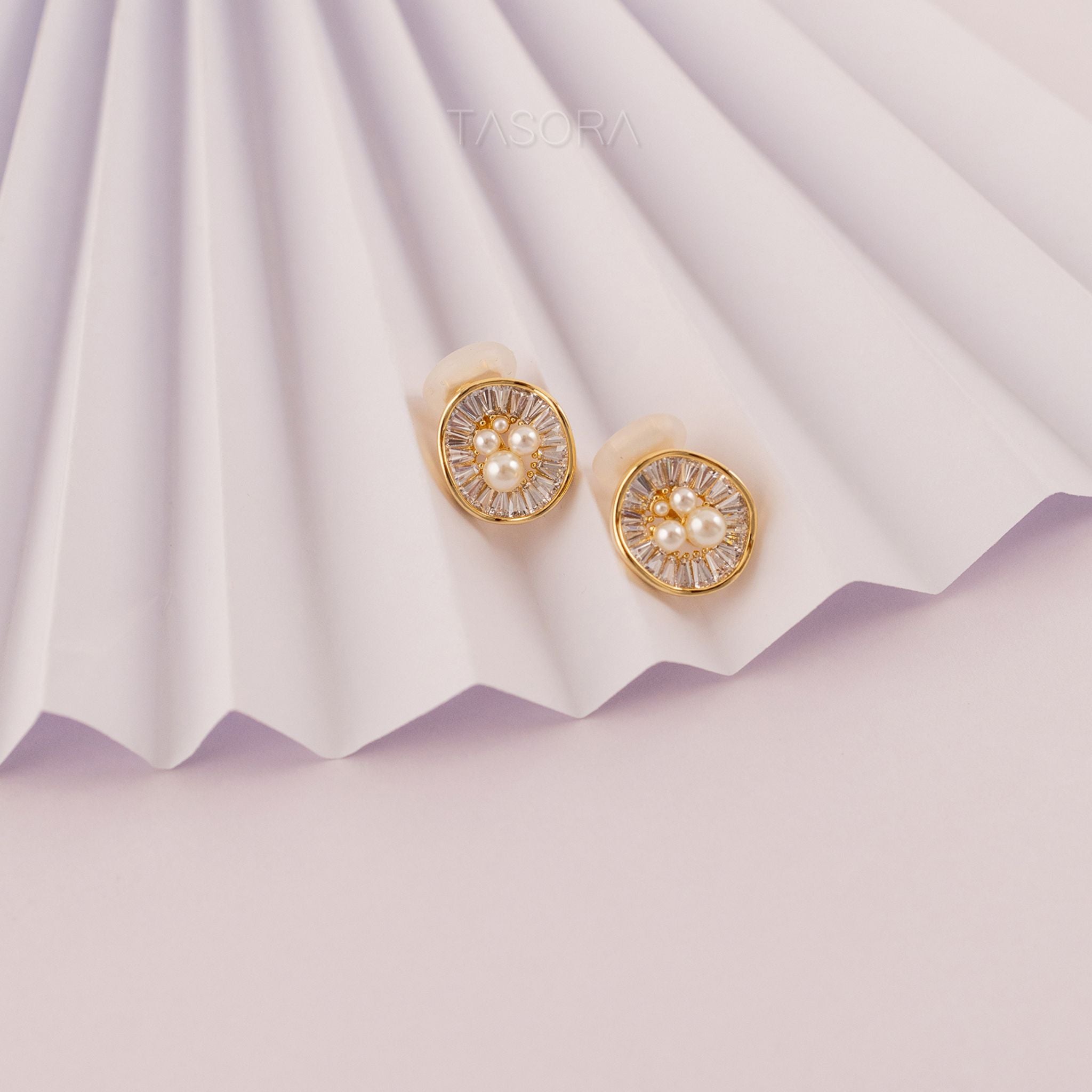 Oyster Muse Golden earrings with pearl on a white pleated paper background with TASORA branding