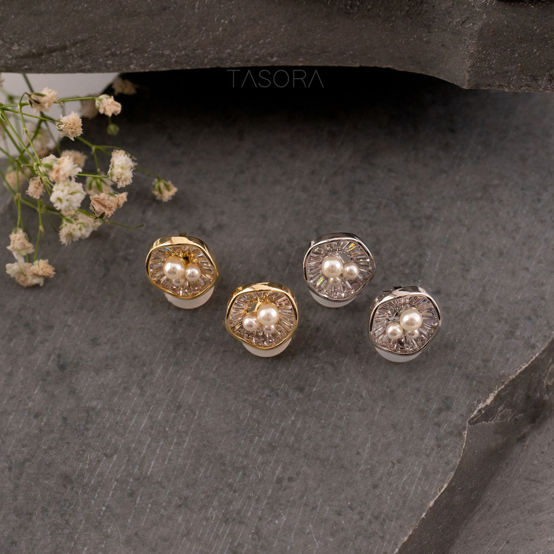 Gold and silver Oyster Muse earrings with pearls on a dark stone surface, TASORA brand visible.
