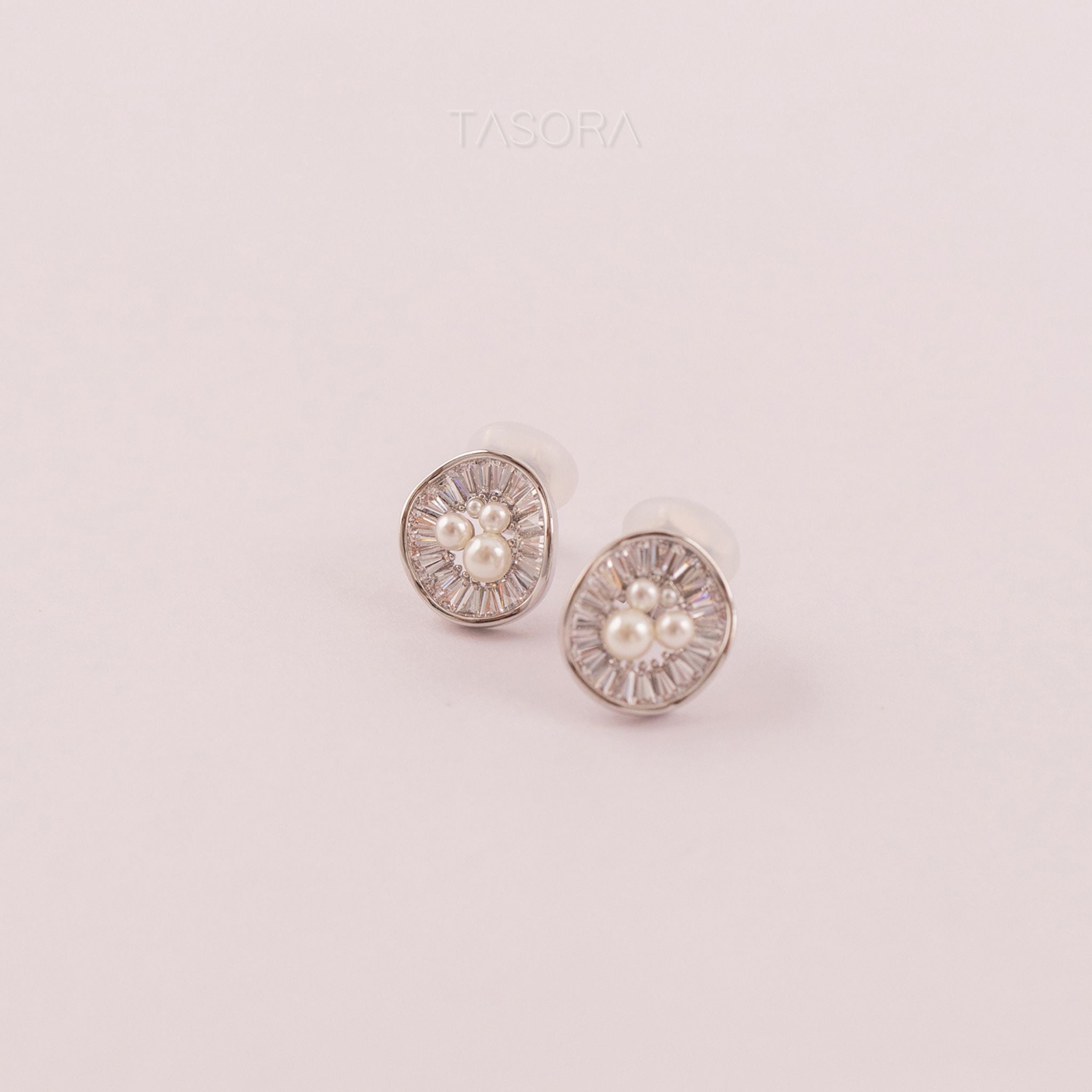 Pair of round Oyster Muse silver earrings with pearls on a light pink background, featuring the brand 'TASORA'.
