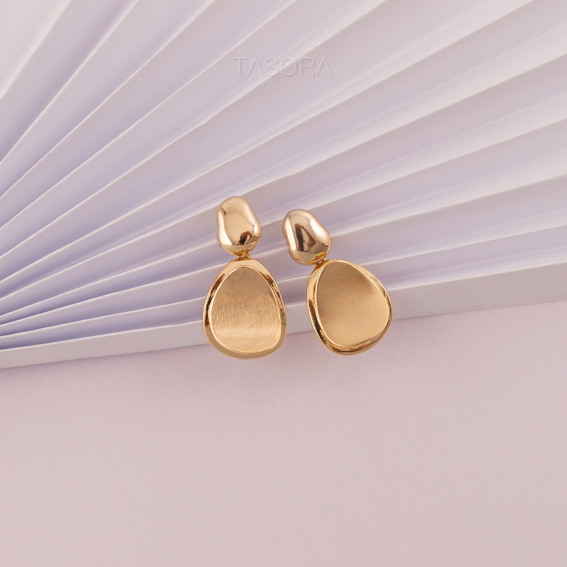 Gold Pebble Huggie earrings on a textured white surface with 'TASORA' branding.