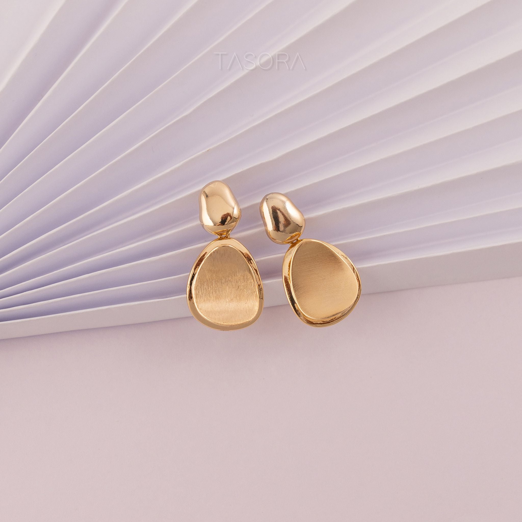 Gold Pebble Huggie earrings on a textured white surface with 'TASORA' branding.