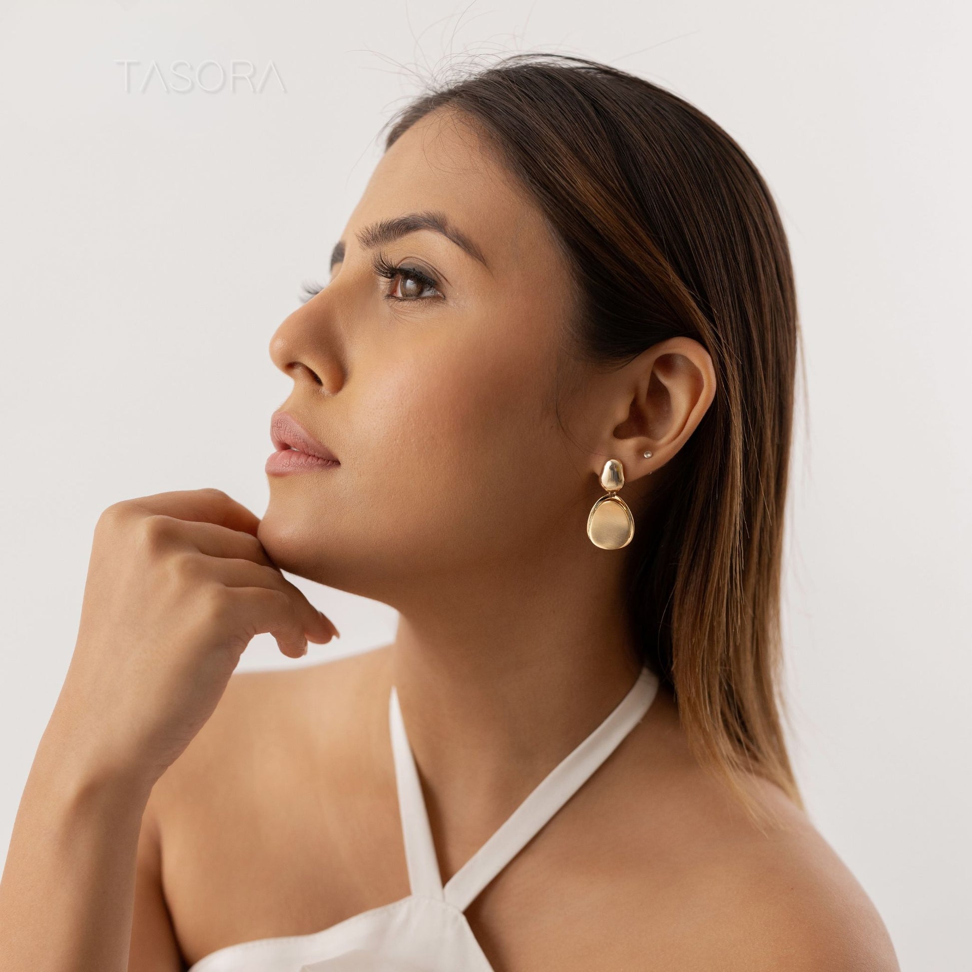 Woman wearing Pebble Huggie Golden earrings of TASORA brand with a plain background