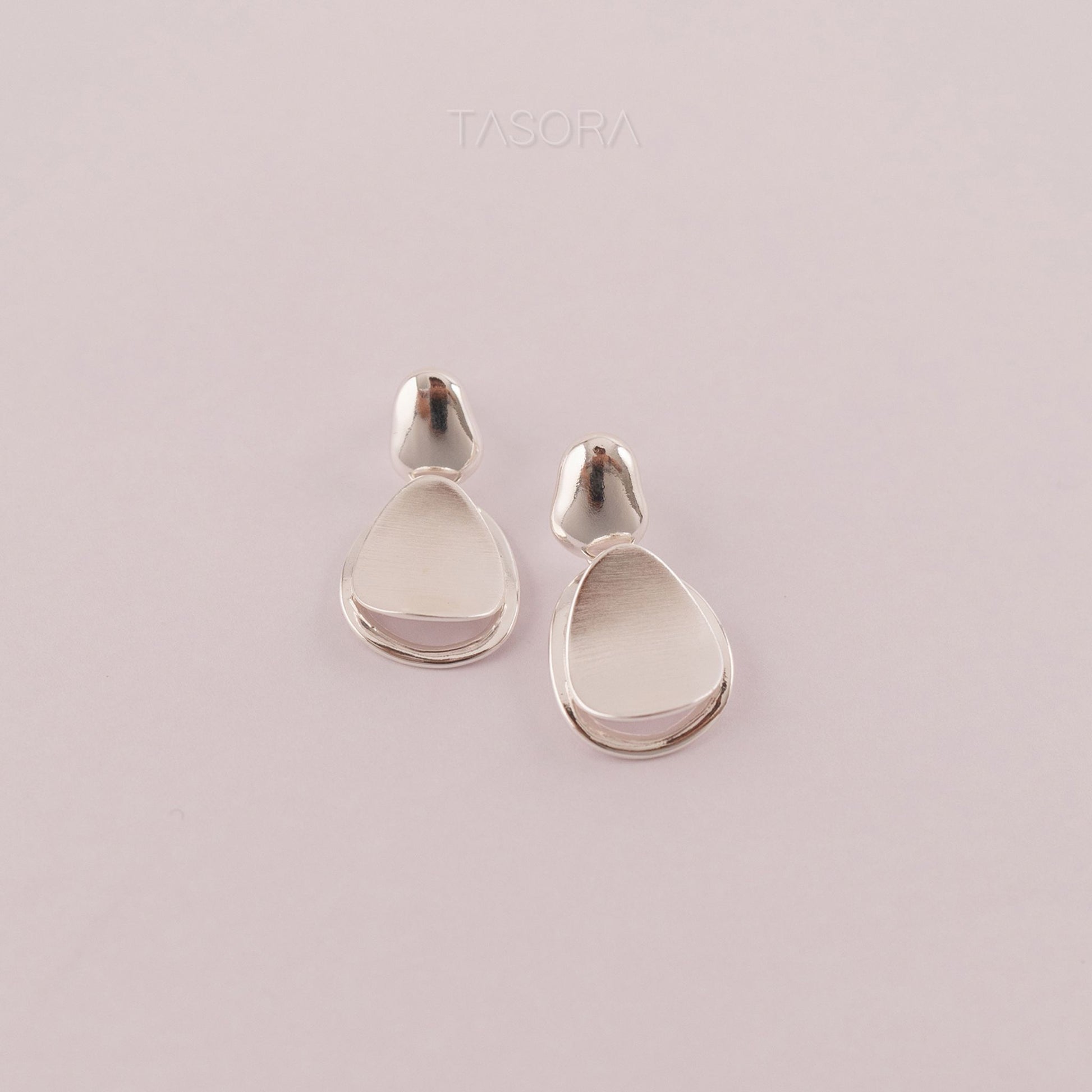 Pebble Huggie silver earrings with light natural background with TASORA branding