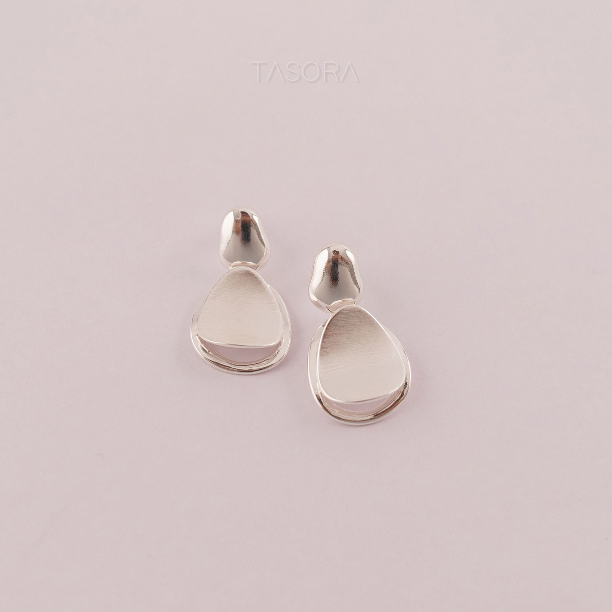 Pebble Huggie silver earrings with light natural background with TASORA branding
