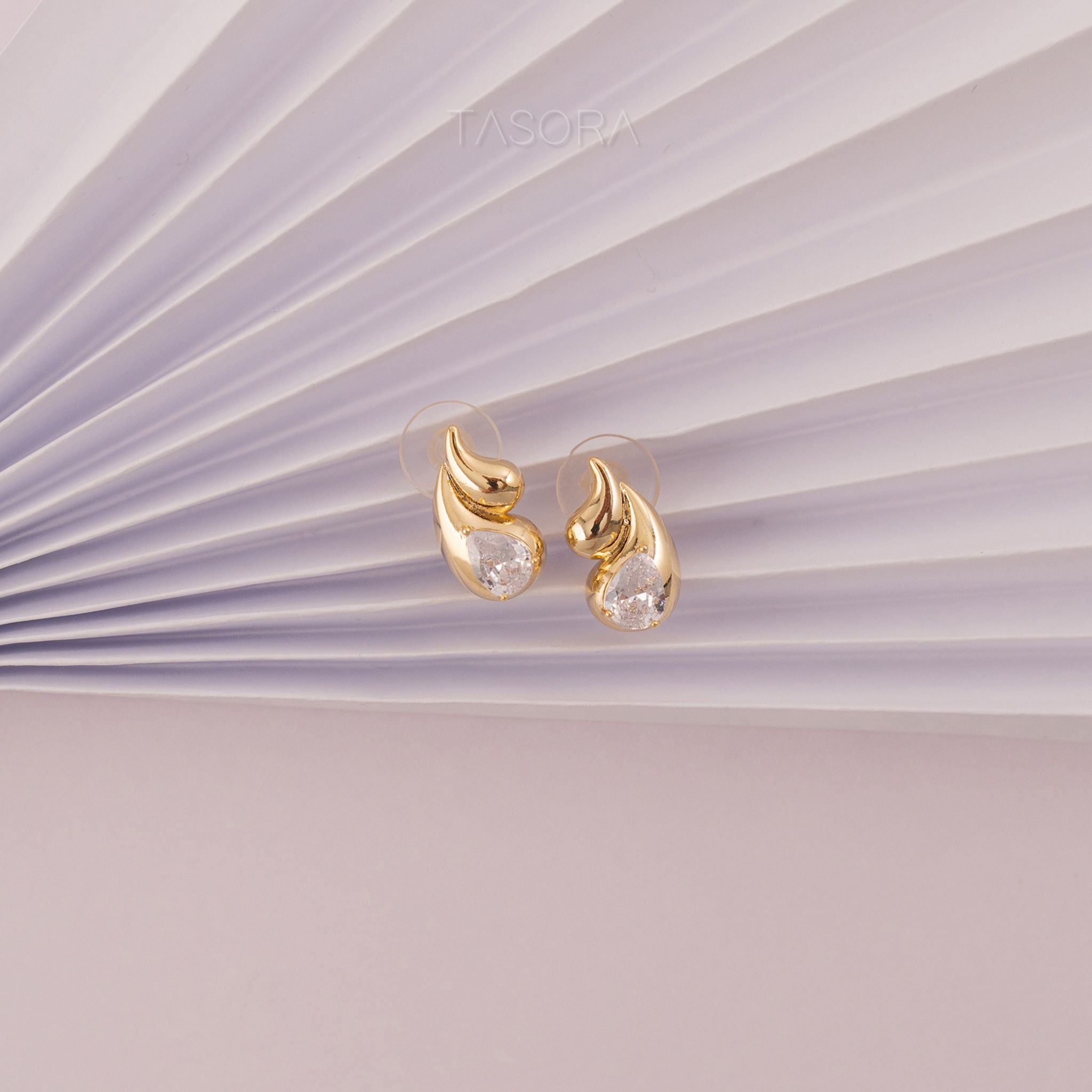 Rain Drop Golden earrings with clear stones on a light purple background with TASORA brand