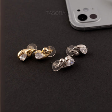 Pair of Rain Drop golden and silver earrings on a dark surface with a phone and TASORA branding in the background.